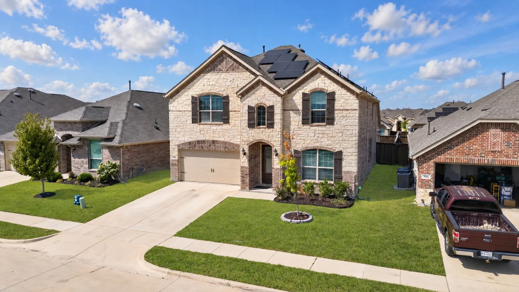 Two-story residence featuring stone and brick exterior, dark shutters, an attached garage, solar panels, and a well-maintained lawn