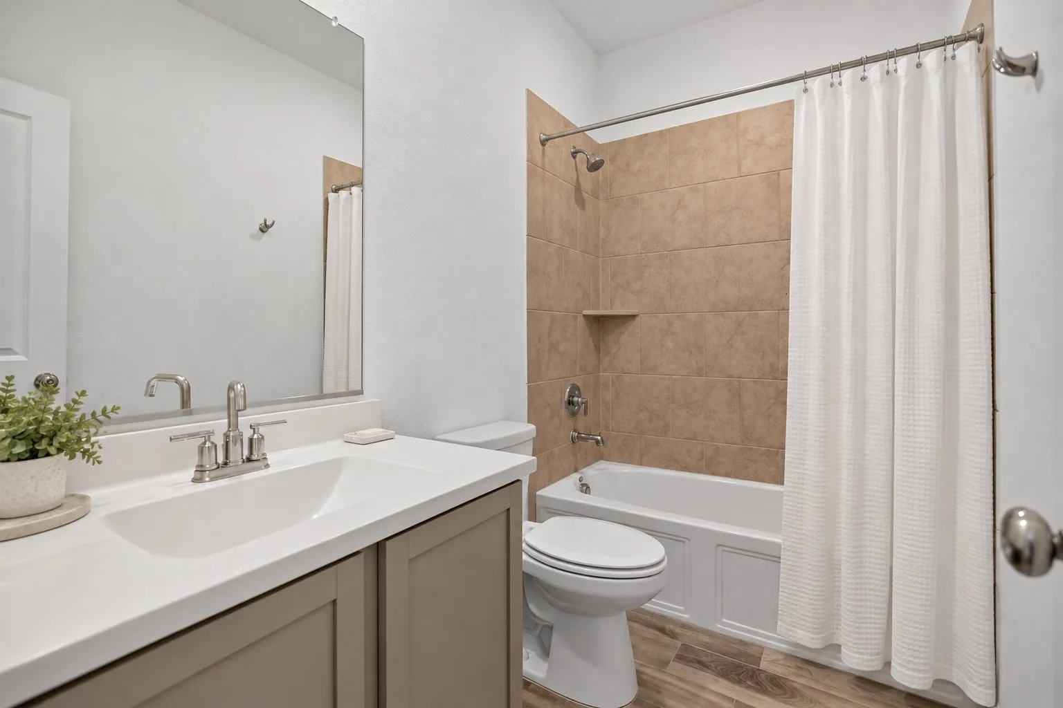 Bathroom featuring a vanity with a white countertop and brushed nickel faucet, a white toilet, a shower/tub combination with beige tile surround, and wood-finish flooring
