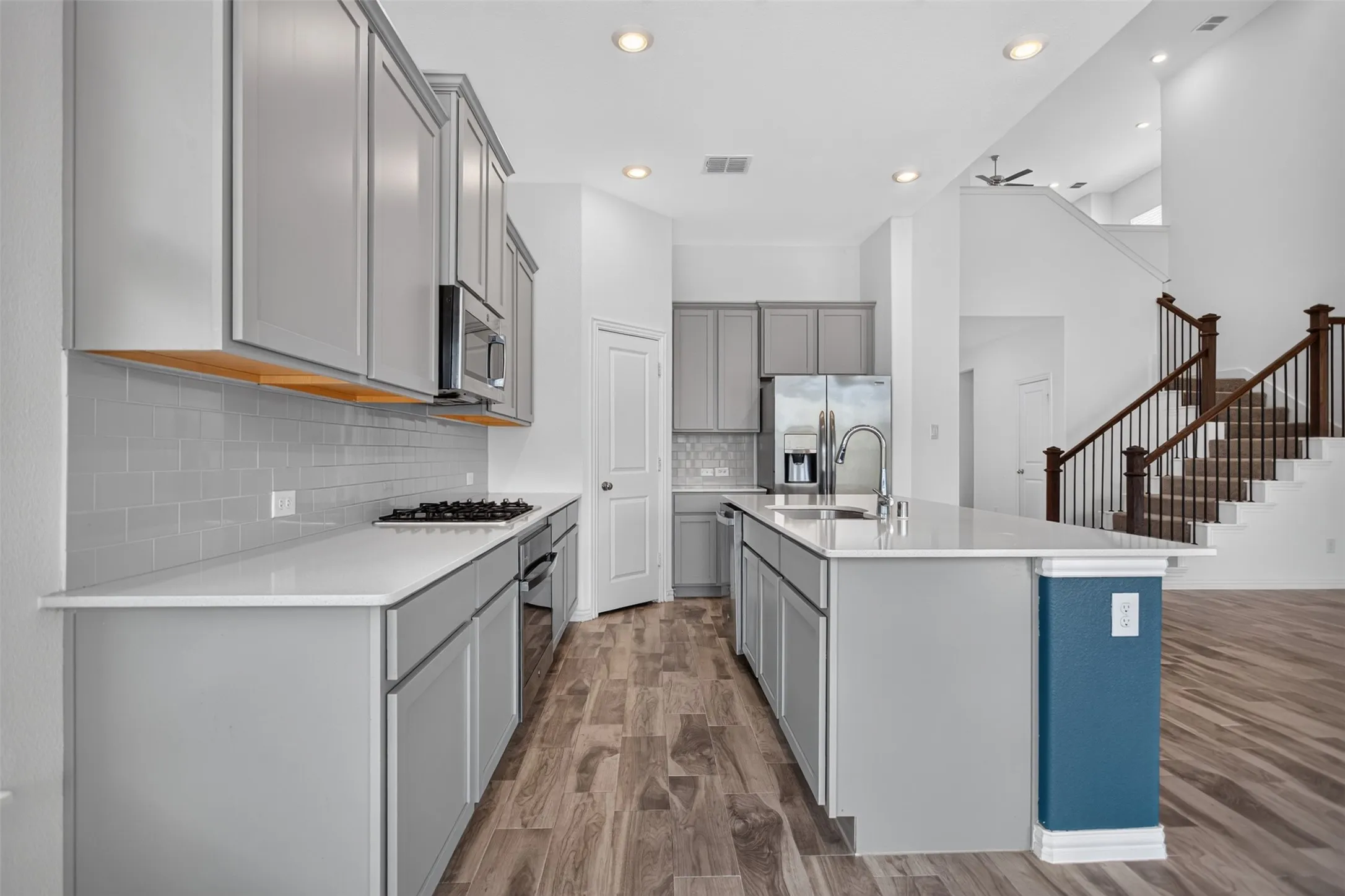 Modern kitchen featuring light gray cabinetry, white countertops, stainless steel appliances, and wood-finish flooring