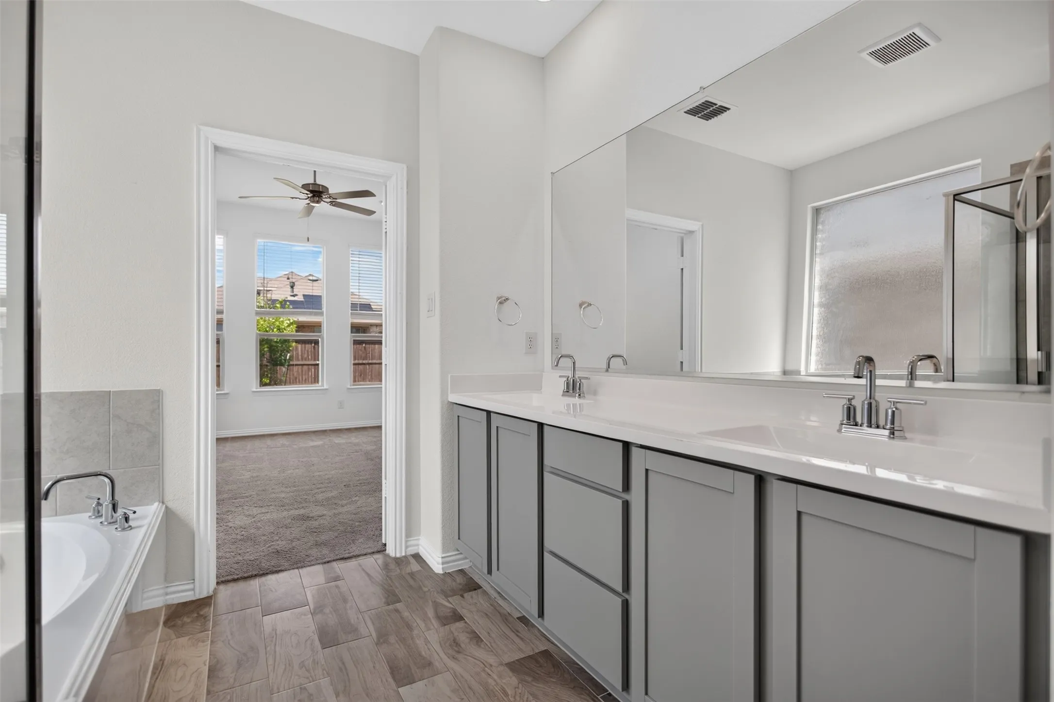 Dual vanity with white countertops, wood-finish tile flooring, recessed lighting, and a built-in tub