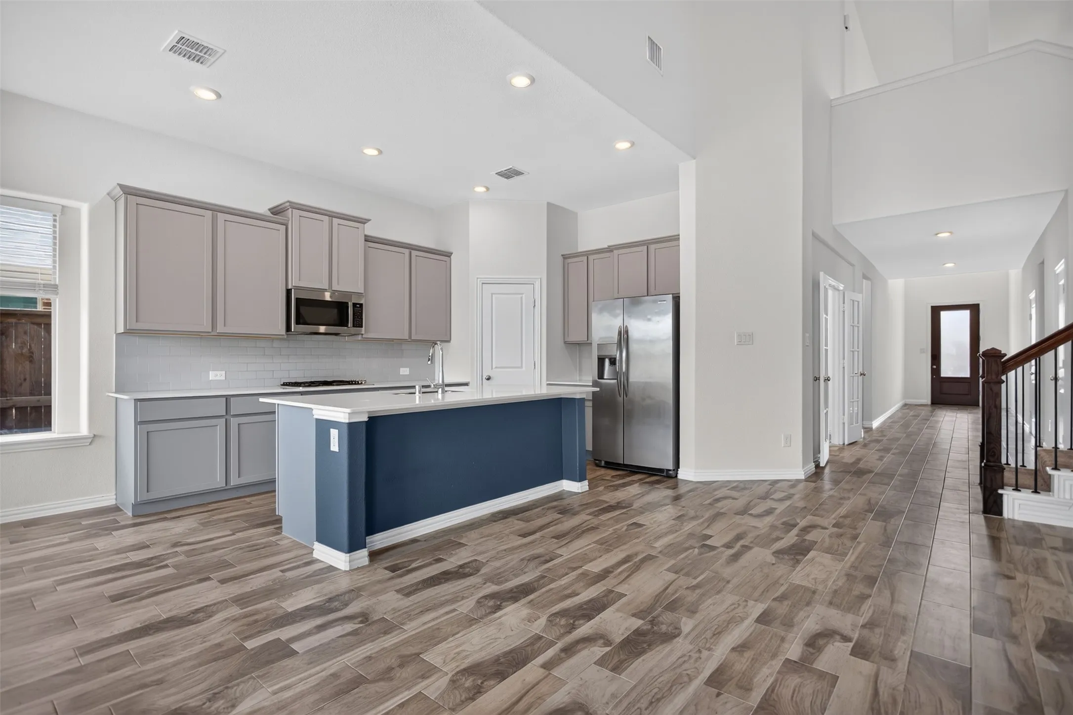 Open-concept kitchen featuring an island with a contrasting base, light gray cabinetry, stainless steel appliances, and wood-finish flooring