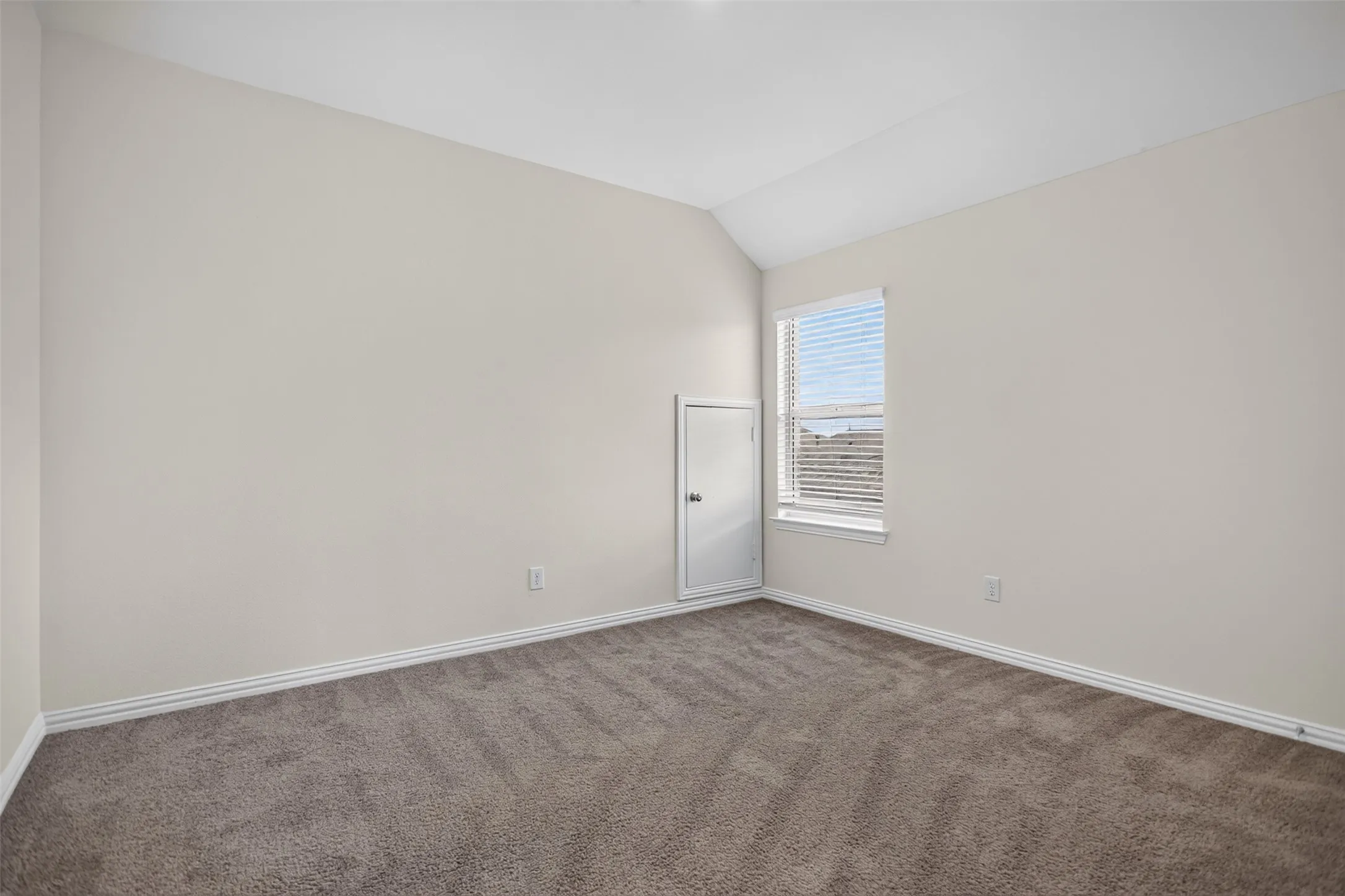 Vaulted ceiling, neutral wall paint, carpeted flooring, window with blinds, white trim