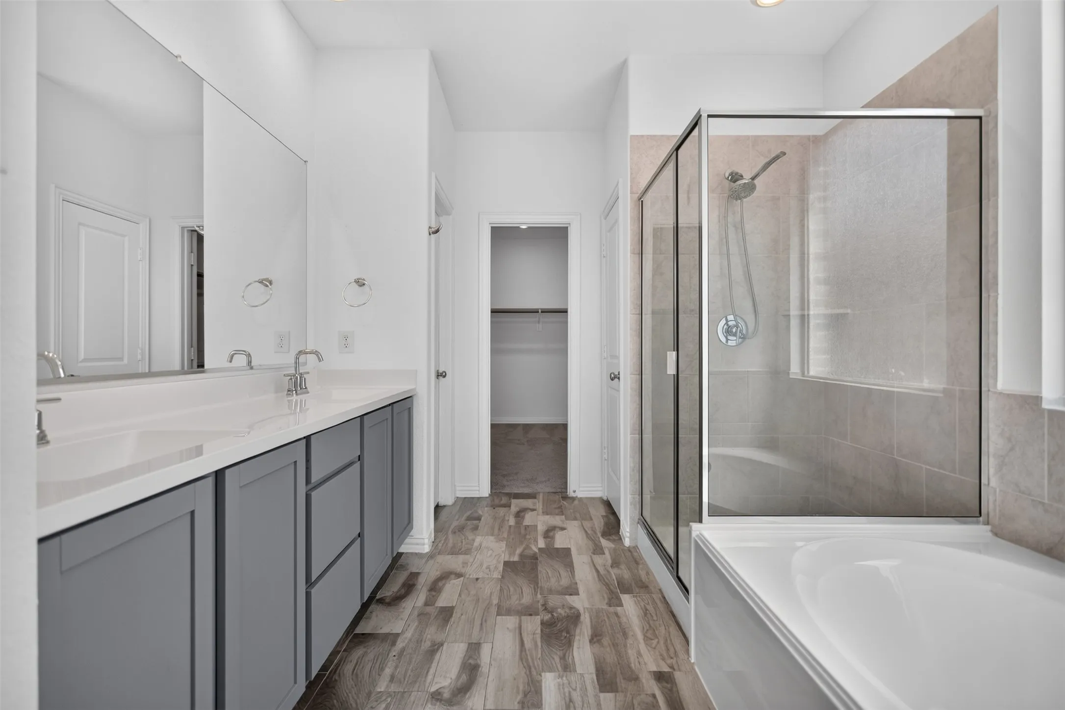 Dual vanity with undermount sinks, full-width mirror, wood-finish flooring, glass-enclosed shower, and a built-in tub