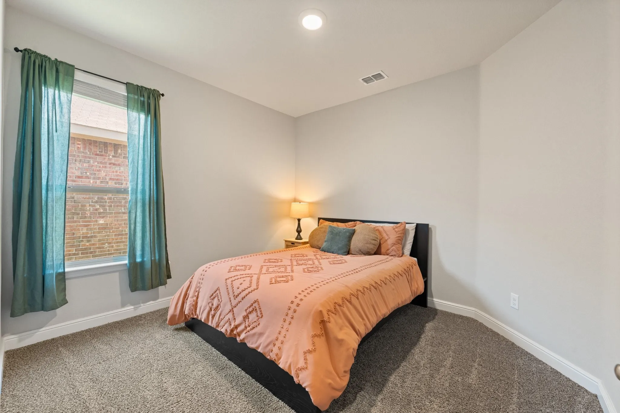 Bright secondary bedroom featuring carpeted flooring, recessed ceiling lighting, and large window with teal curtain panels framing natural light