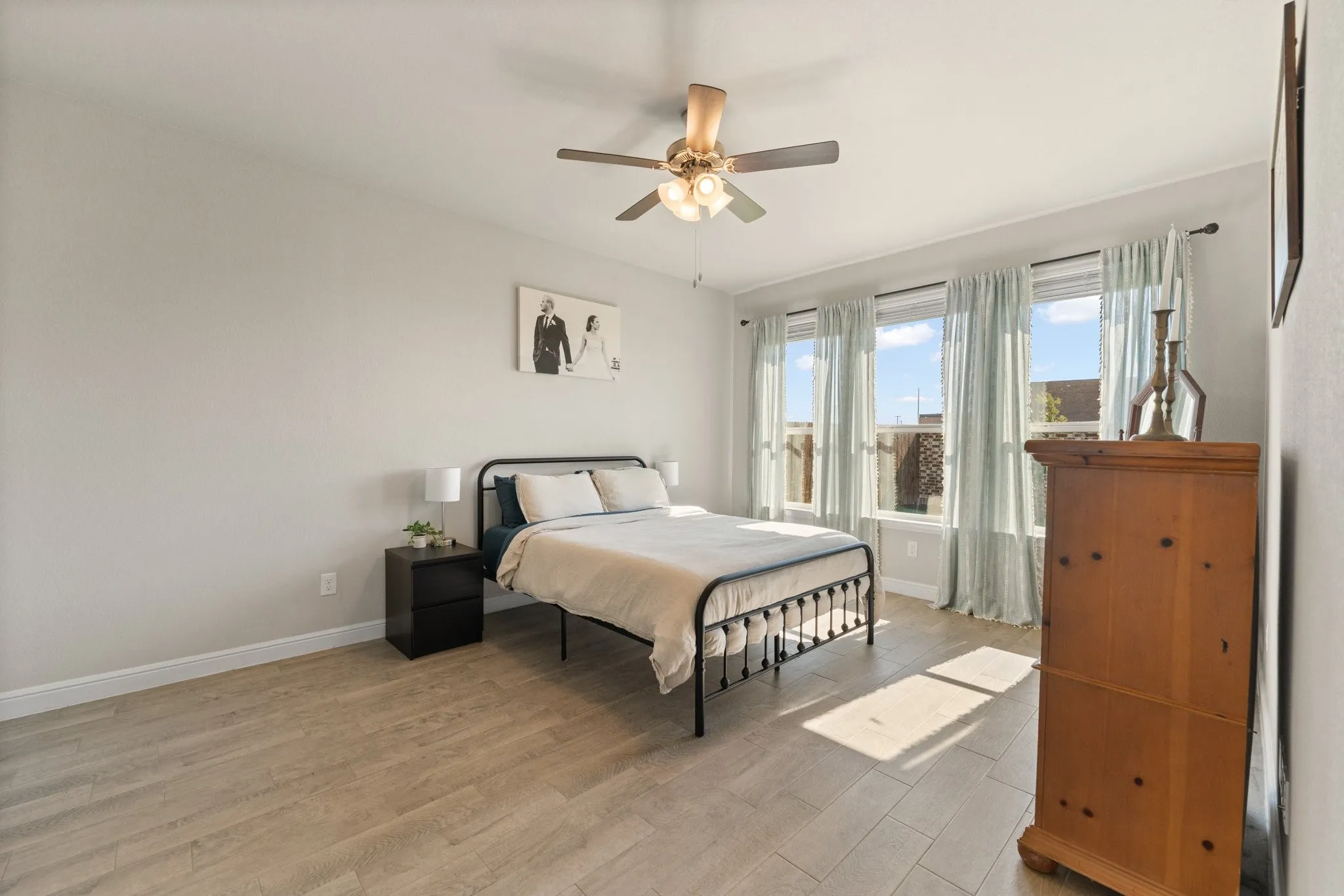Light wood-finish flooring, ceiling fan, and multiple windows with roller shades