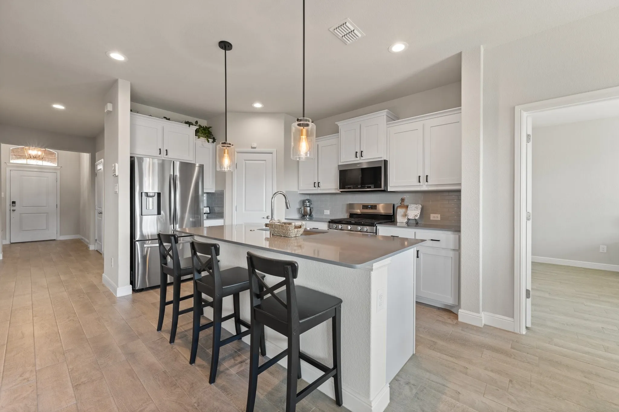 Kitchen island with pendant lighting, stainless steel appliances, white cabinetry, and wood-finish flooring