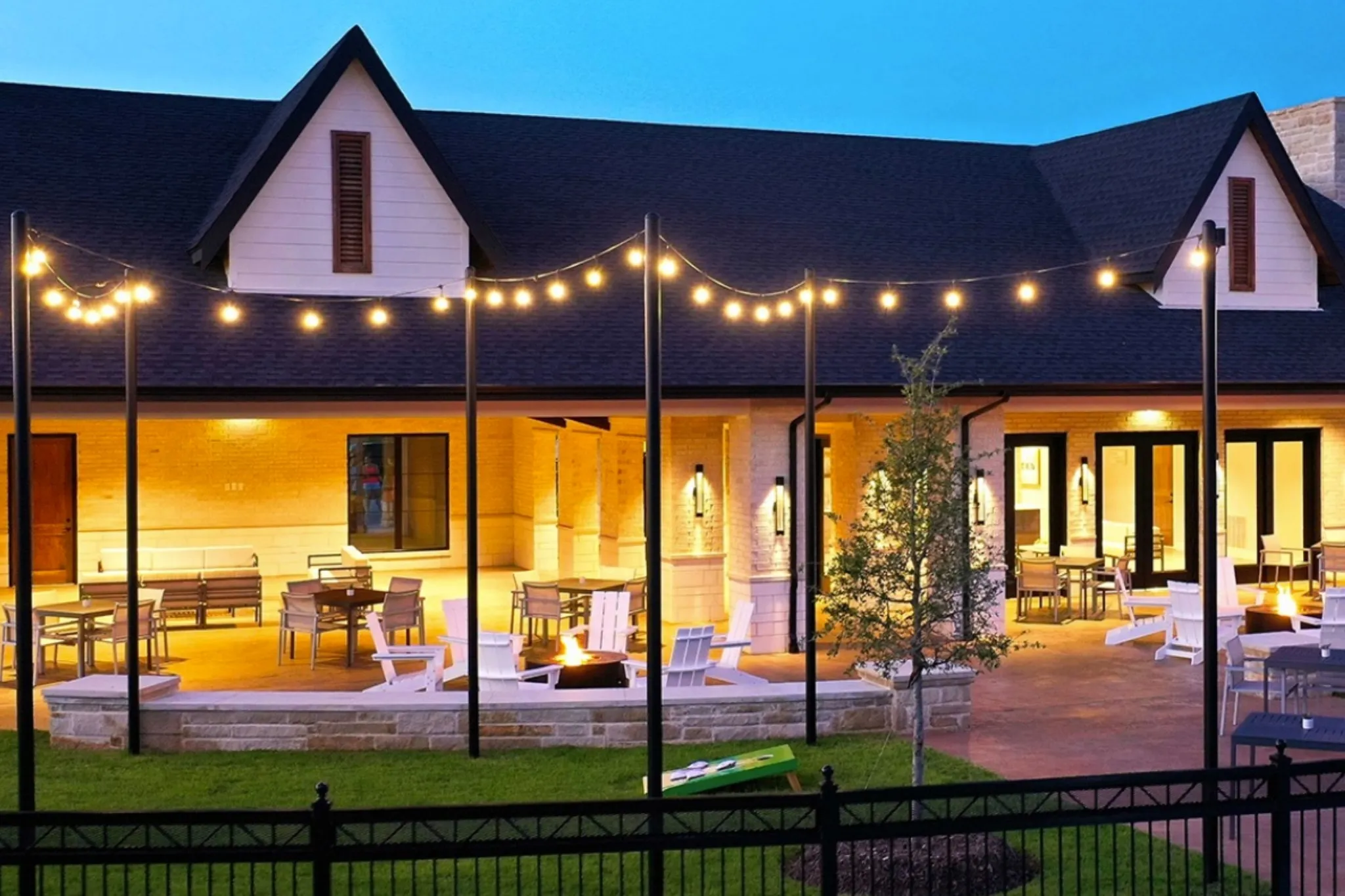 Expansive stone patio featuring a built-in fire pit, string lighting, and multiple points of entry