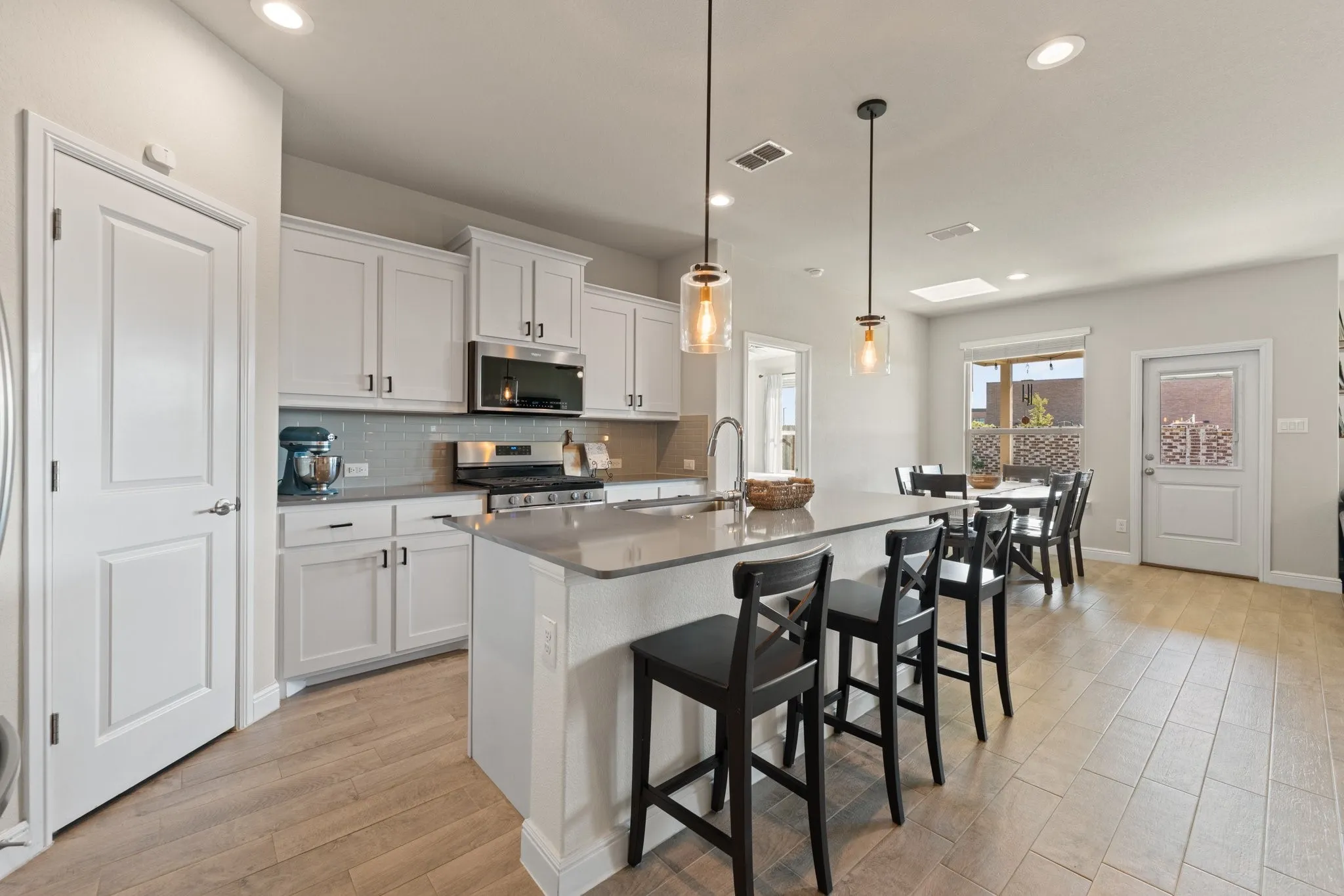Kitchen featuring white cabinetry, stainless steel appliances, a light-toned backsplash, a spacious island with a sink, and wood-finish flooring