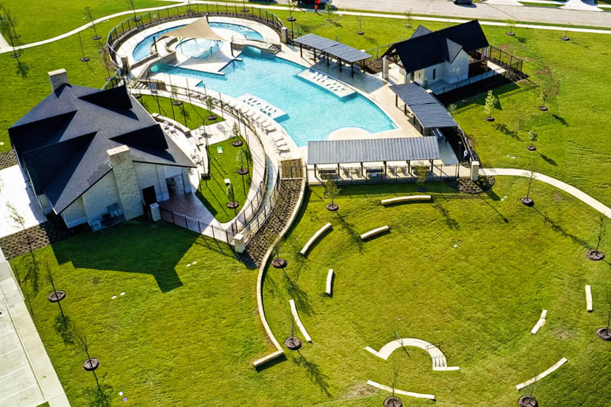 Community swimming pool with sun deck, multiple shaded lounge areas, and adjacent recreational building