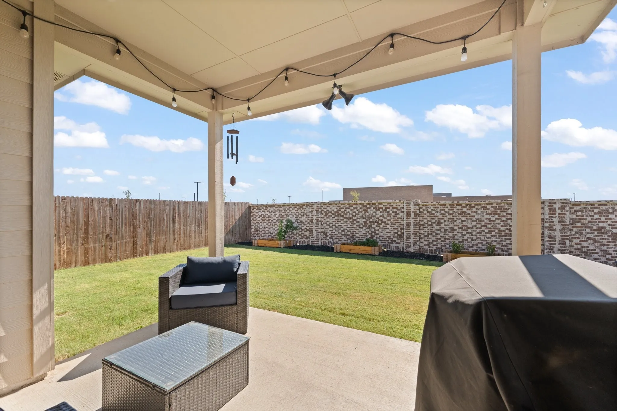 Covered patio with concrete flooring, bordered by a wood fence and a brick privacy wall