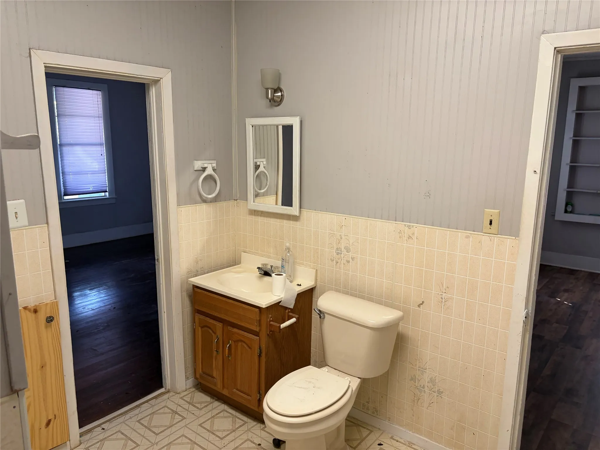 Vanity with wood-finish cabinetry, tile wainscoting, wall-mounted light fixture, and a mirror