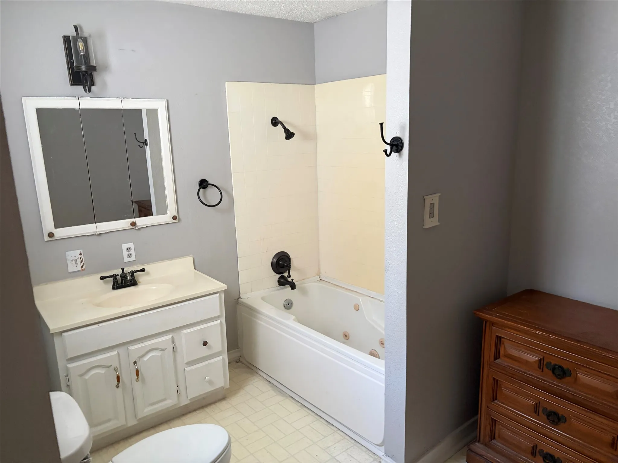 White vanity with a single sink, medicine cabinet, jetted bathtub, and tile flooring
