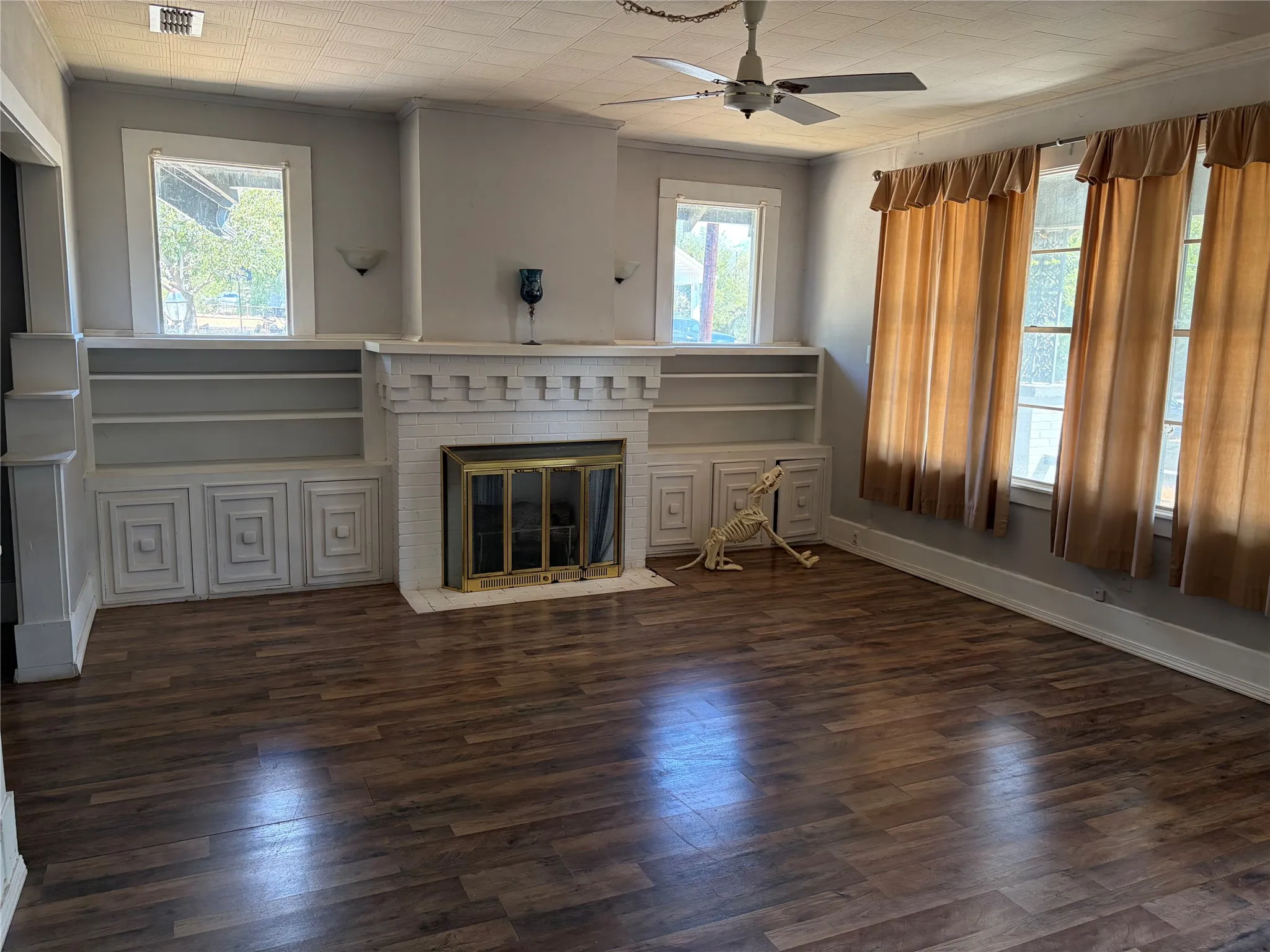 Wood-finish flooring throughout, featuring a white painted fireplace with a brass firebox, flanked by built-in shelving and lower cabinetry