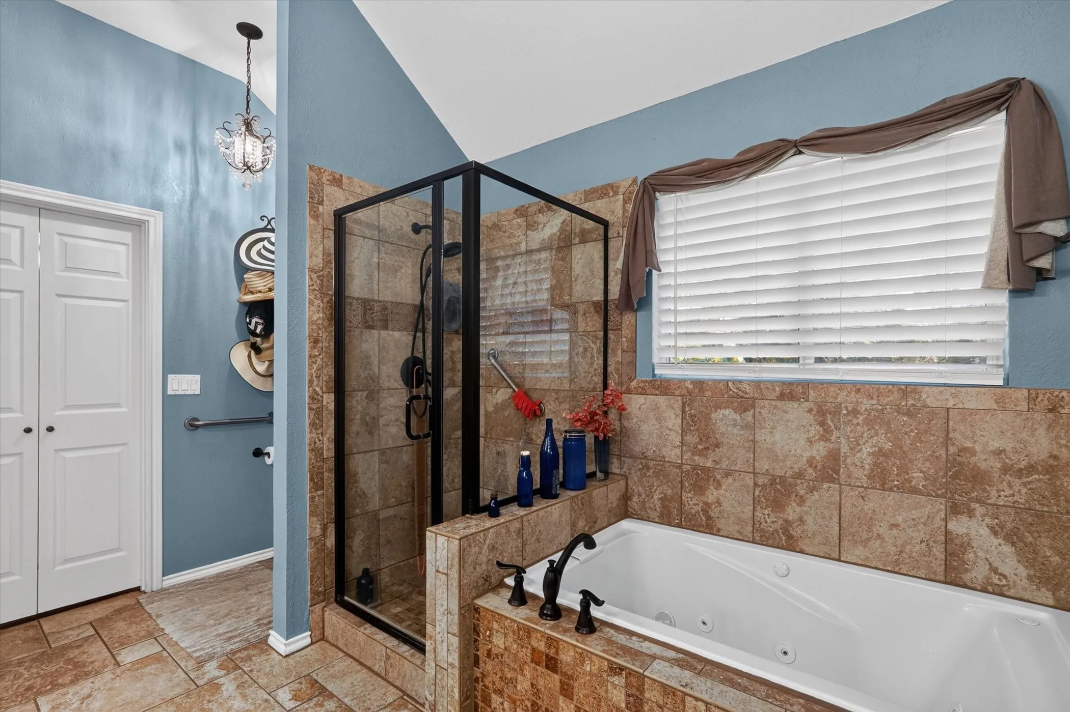 Soaking tub with a tiled surround, a glass-enclosed shower, and a vaulted ceiling with a decorative light fixture