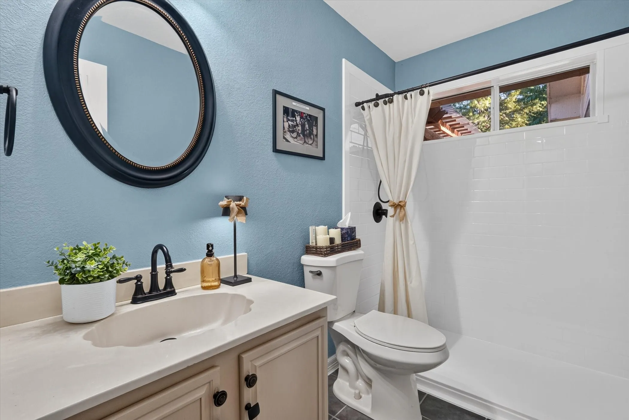 Bathroom featuring a single vanity with an integrated sink, dark bronze-finish hardware, subway tile shower surround, and a fixed window