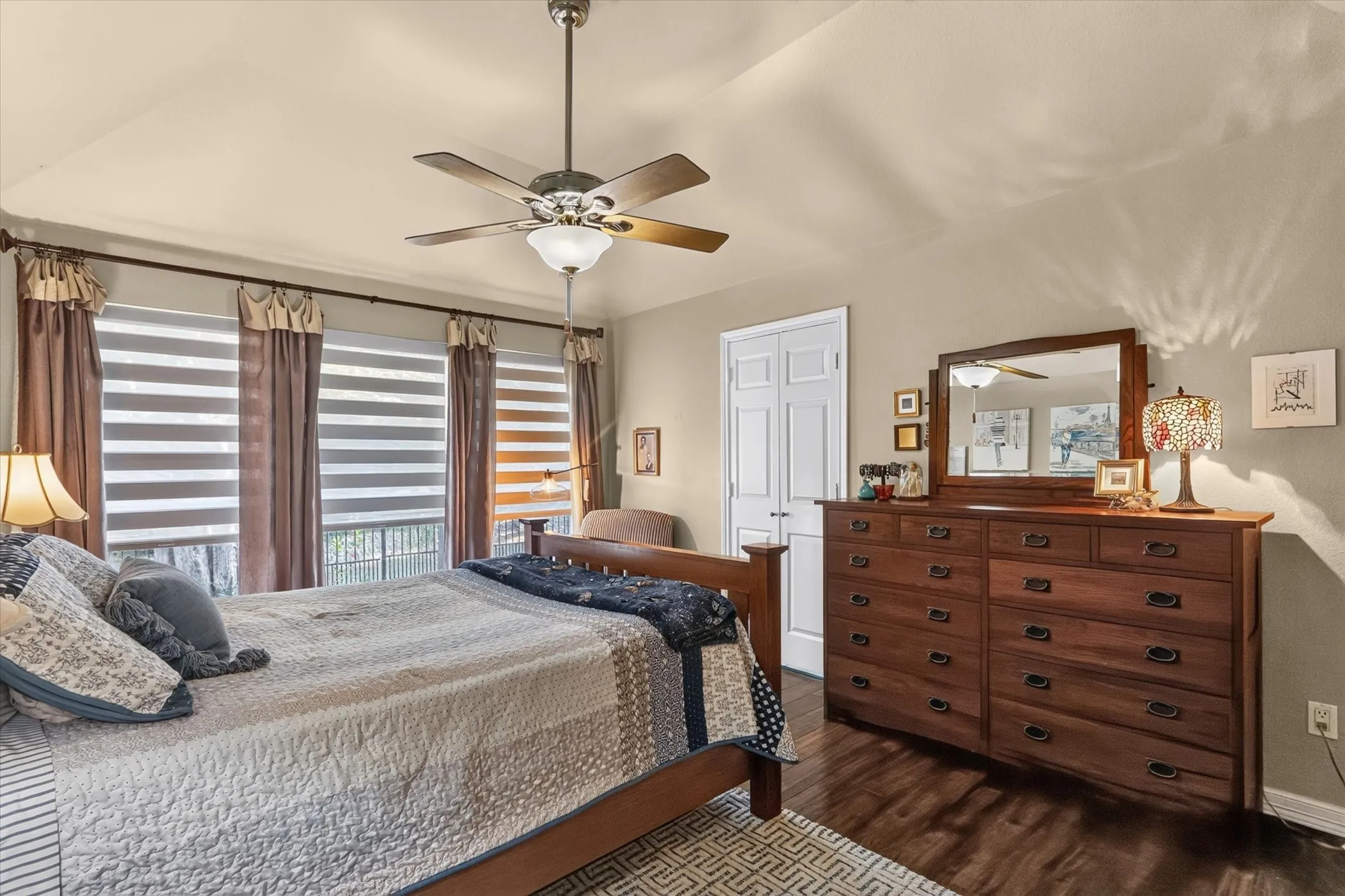 Vaulted ceiling with a ceiling fan, wood-finish flooring, and multiple windows with layered window treatments