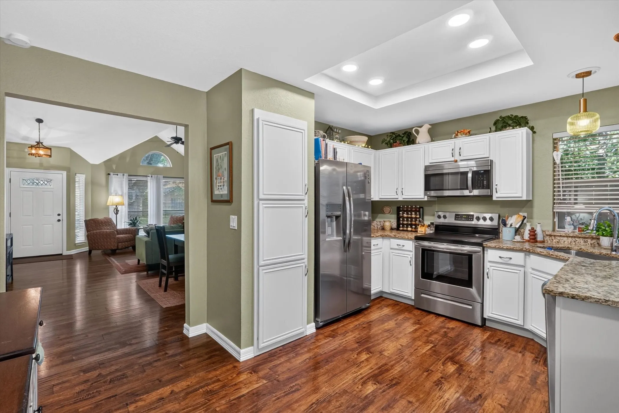 Kitchen featuring stainless steel appliances, white cabinetry, granite-style countertops, wood-finish flooring, and a tray ceiling with recessed lighting
