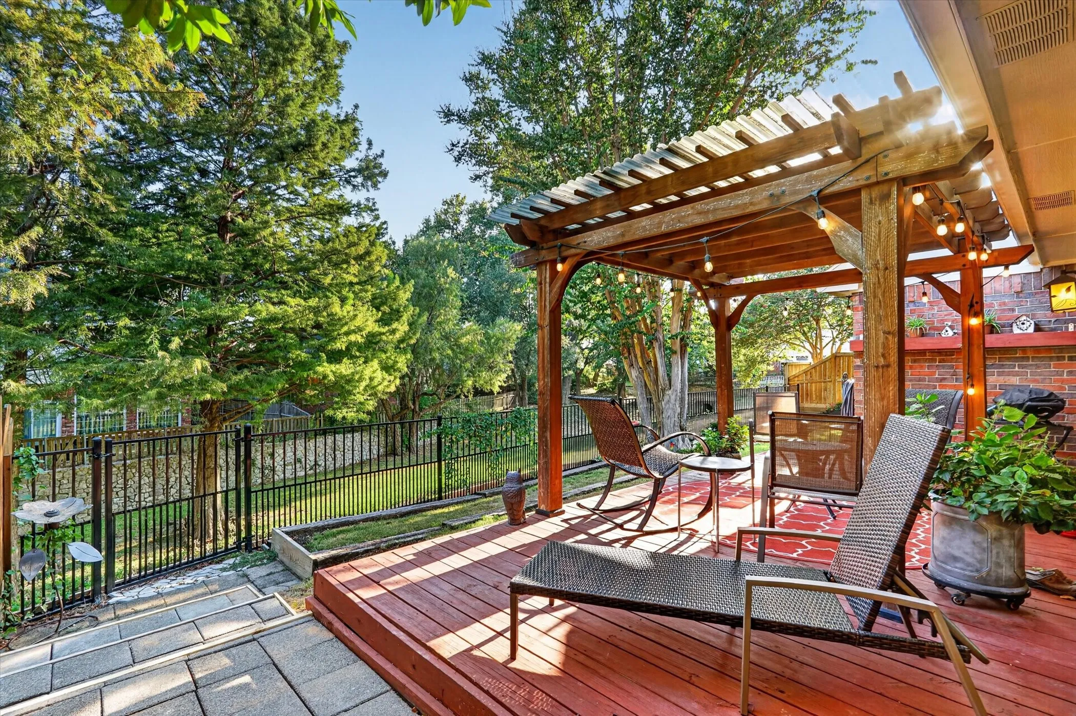 Red-stained wood deck with a built-in wooden pergola, brick retaining wall, and paver steps