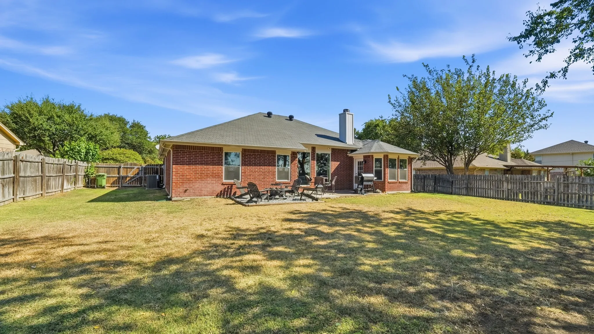 Expansive backyard featuring a brick exterior, a patio with a built-in privacy wall, a shingle roof, and a wood privacy fence