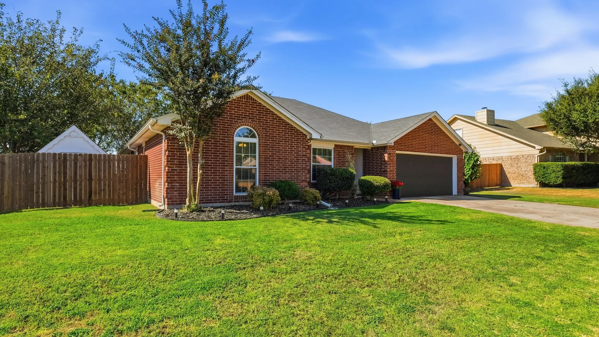 Traditional brick exterior, attached garage, arched window, mature landscaping, and a fenced yard