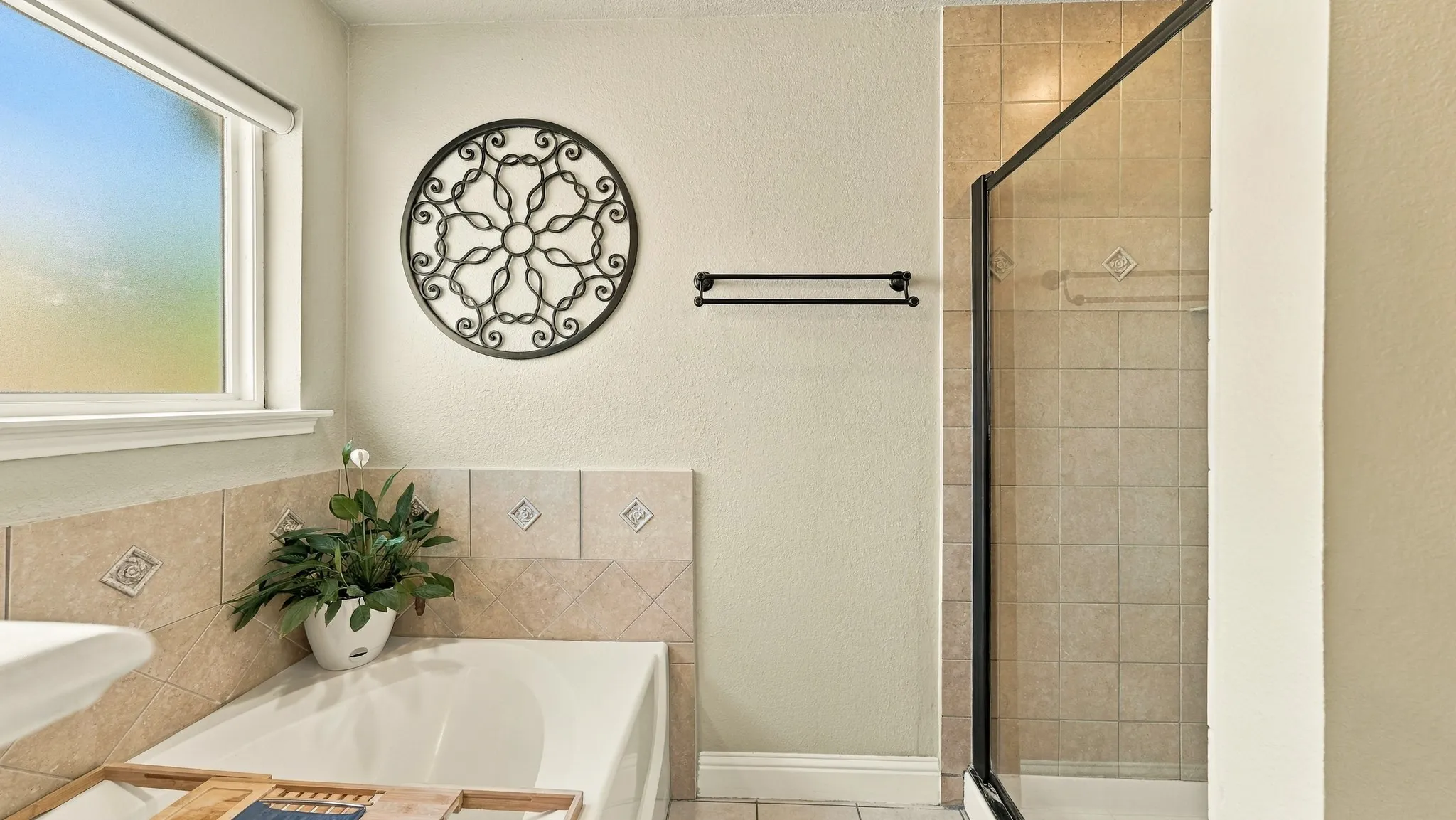 Recessed bathtub with a tiled surround featuring decorative inserts, accompanied by a separate glass-enclosed shower with tiled walls