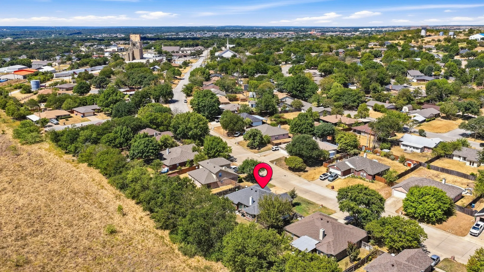 Aerial depiction of a residential neighborhood with established homes, mature trees, and a prominent steeple in the background