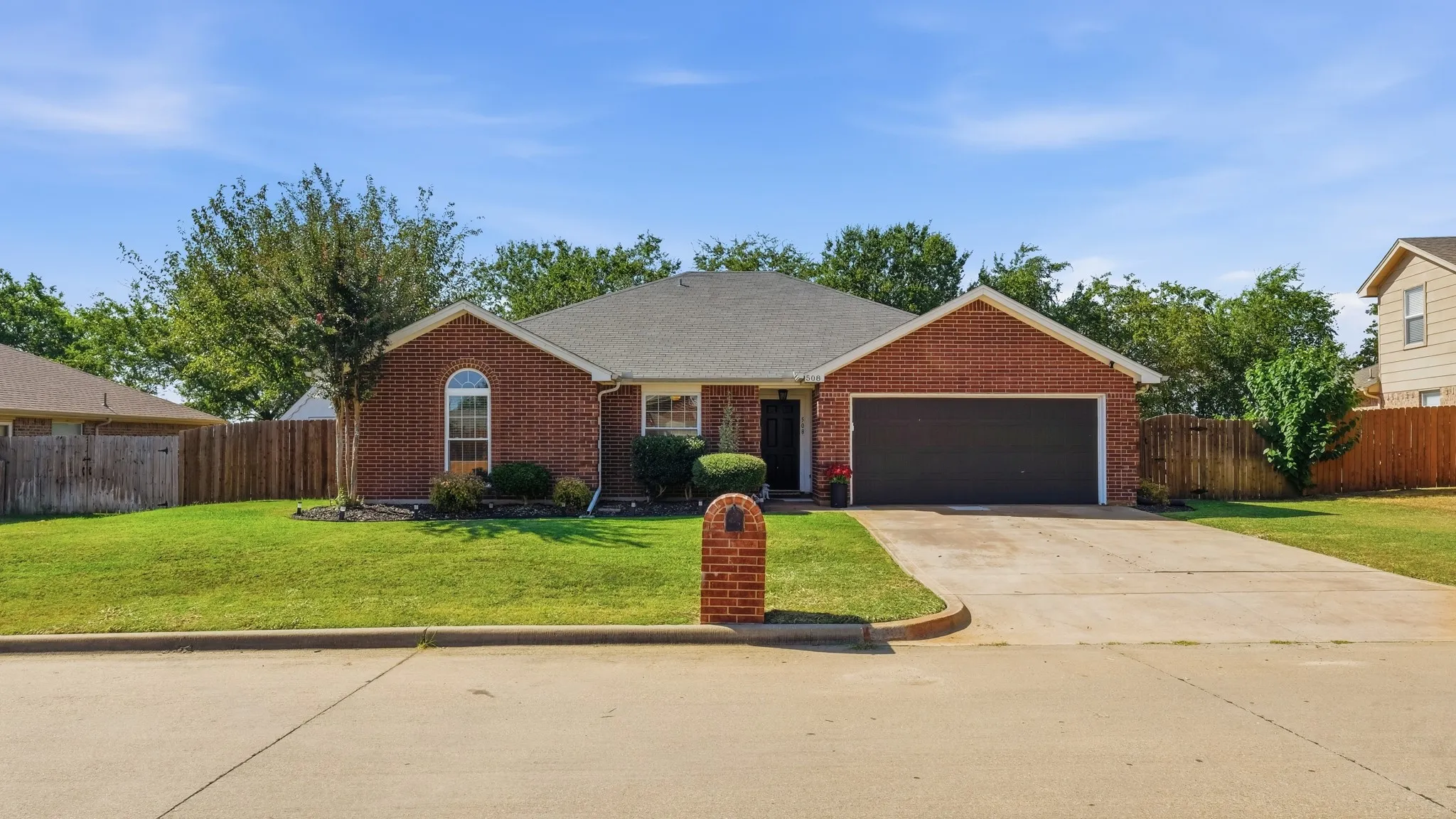Brick exterior with a two-car garage, concrete driveway, arched window, and a fenced perimeter
