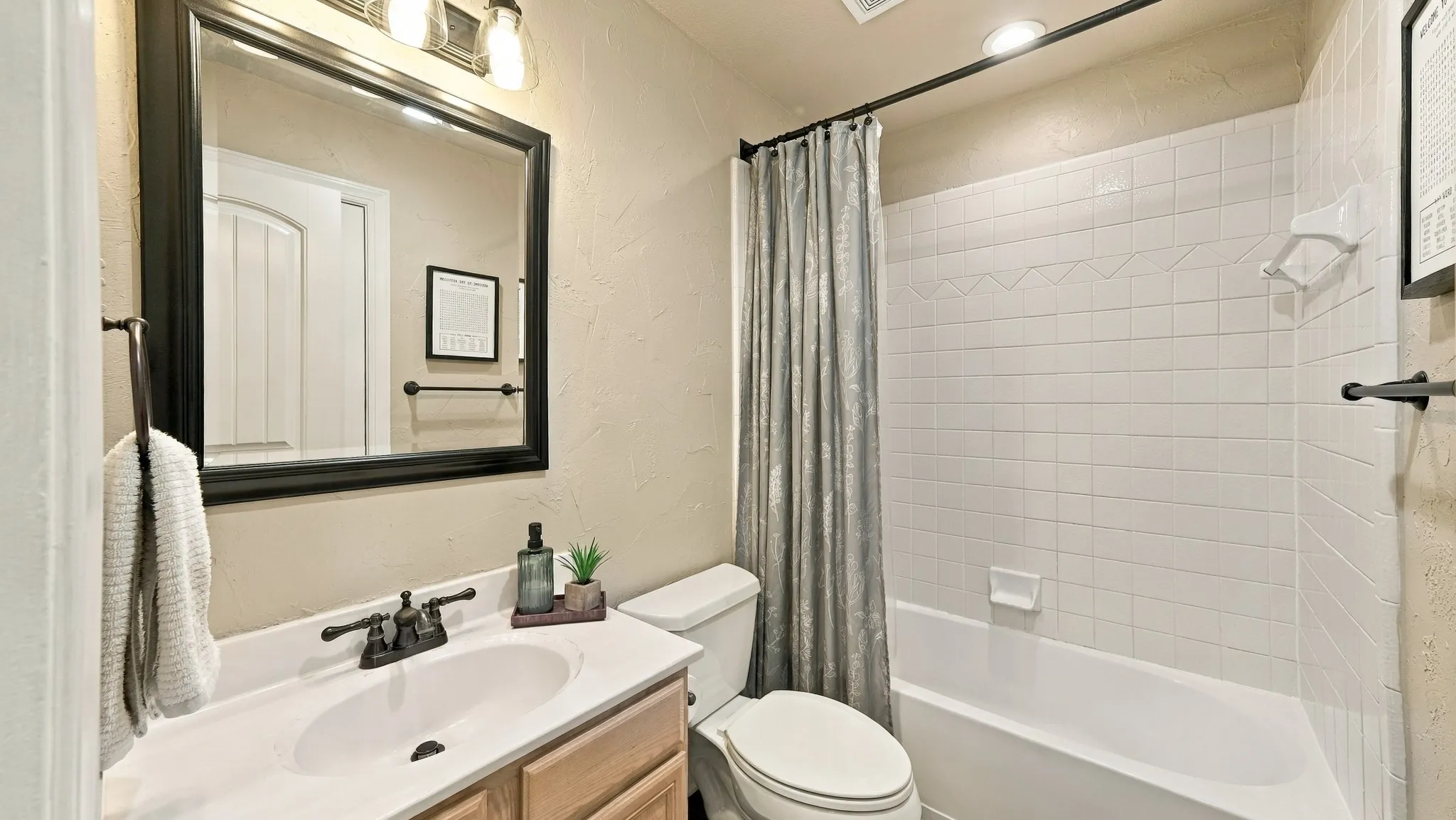 Bathroom with a light-toned vanity, white countertop, dark-toned framed mirror, and a tiled shower-tub combination