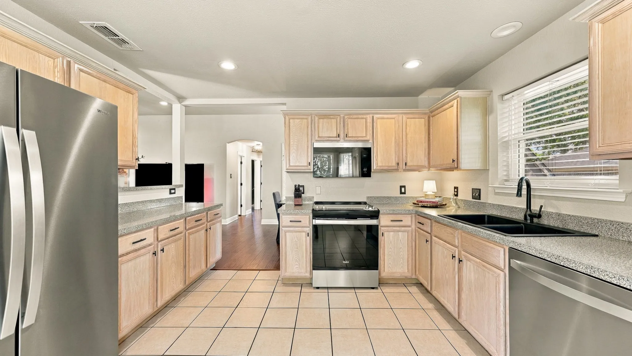 Kitchen featuring light wood-finish cabinetry, light speckled countertops, stainless steel appliances, a black sink, and tile flooring