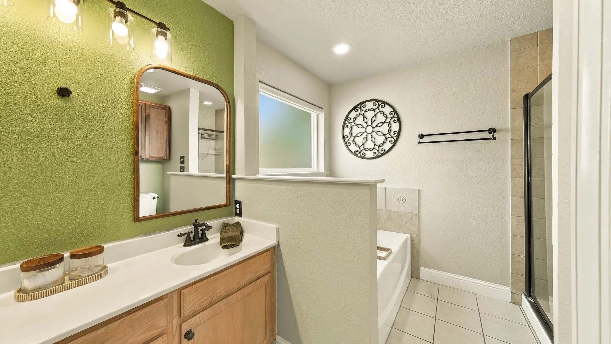 Vanity with wood-finish cabinetry and light-toned countertop, framed mirror, built-in bathtub, and a separate shower enclosure