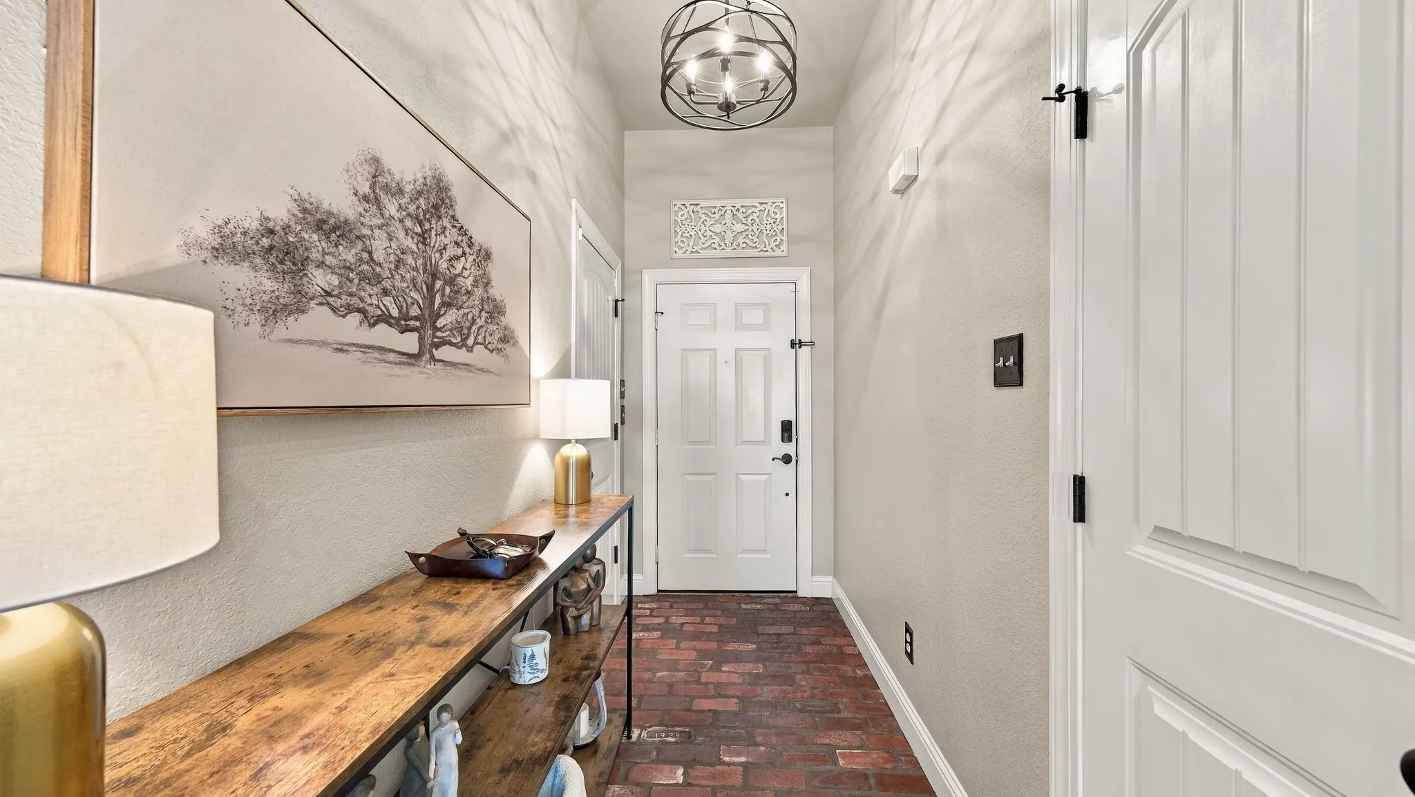 Brick-pattern flooring, white paneled entrance door, and a decorative pendant light fixture