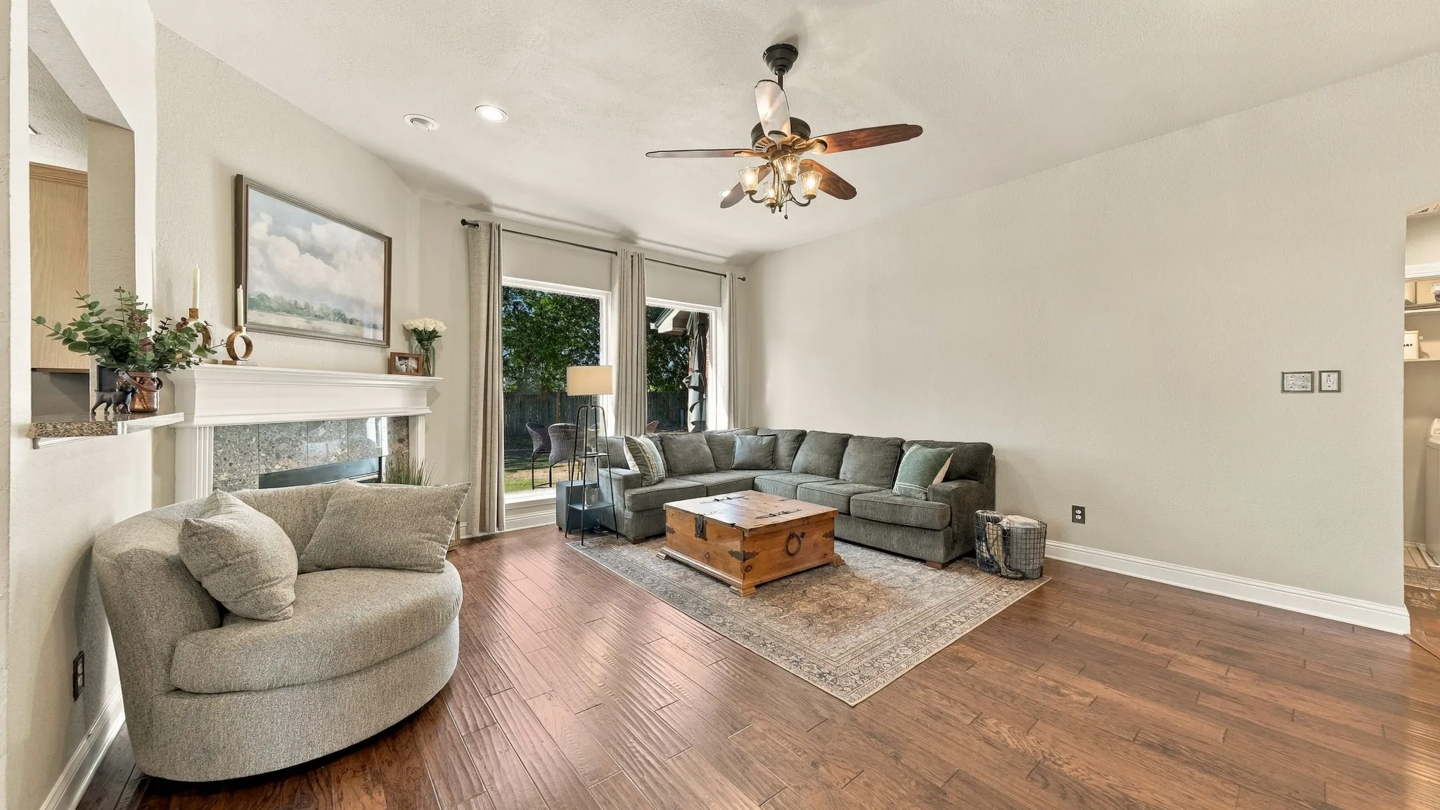 Wood-finish flooring, white mantel fireplace, recessed lighting, ceiling fan with light fixture, and multiple windows