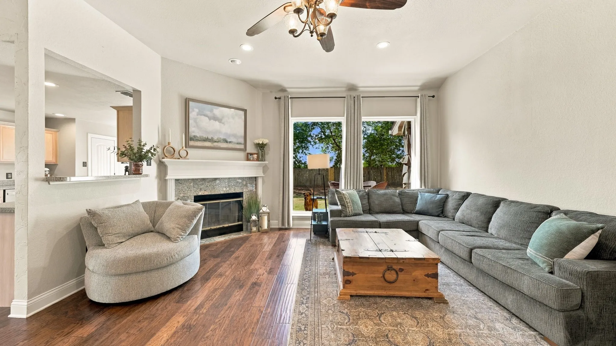 Wood-finish flooring, fireplace with stone surround, recessed lighting, ceiling fan, and large windows