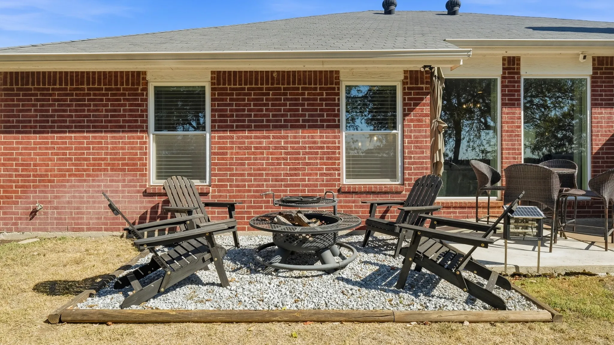 Red brick exterior with white trim, gray shingle roof, and a concrete patio