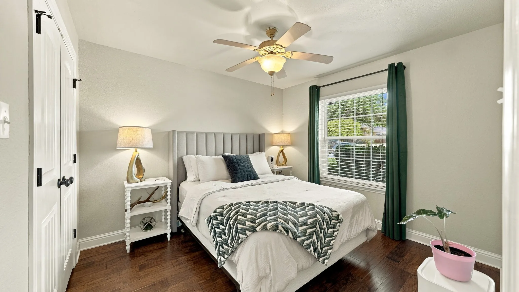 Wood-finish flooring with light-toned walls, a window with horizontal blinds, and a ceiling fan with integrated lighting