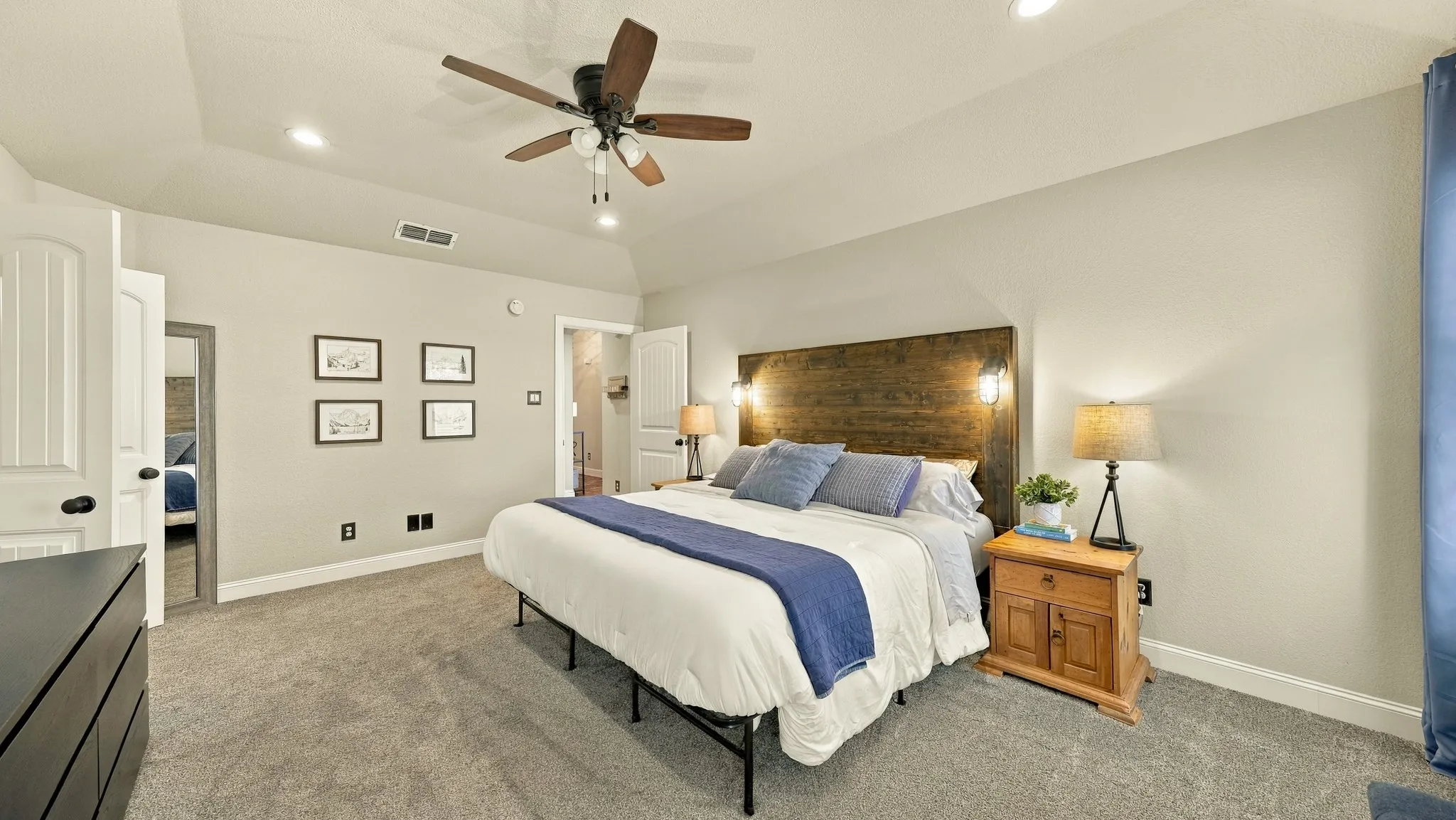 Vaulted ceiling with recessed lighting and a ceiling fan, carpeted flooring, and a wood-finish headboard with integrated sconce lighting