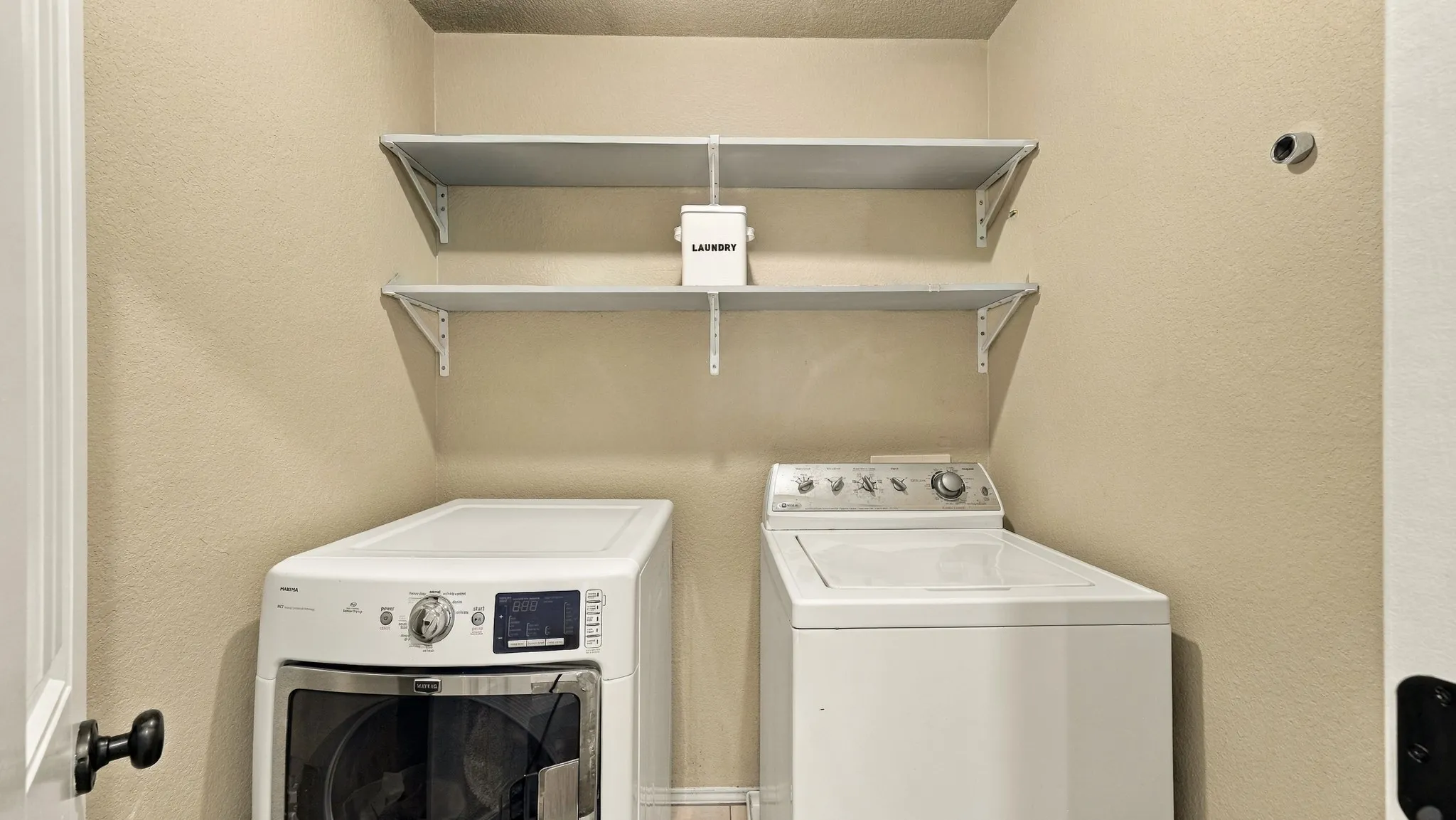 Dedicated laundry area featuring a front-load washer, top-load washer, and two wall-mounted storage shelves