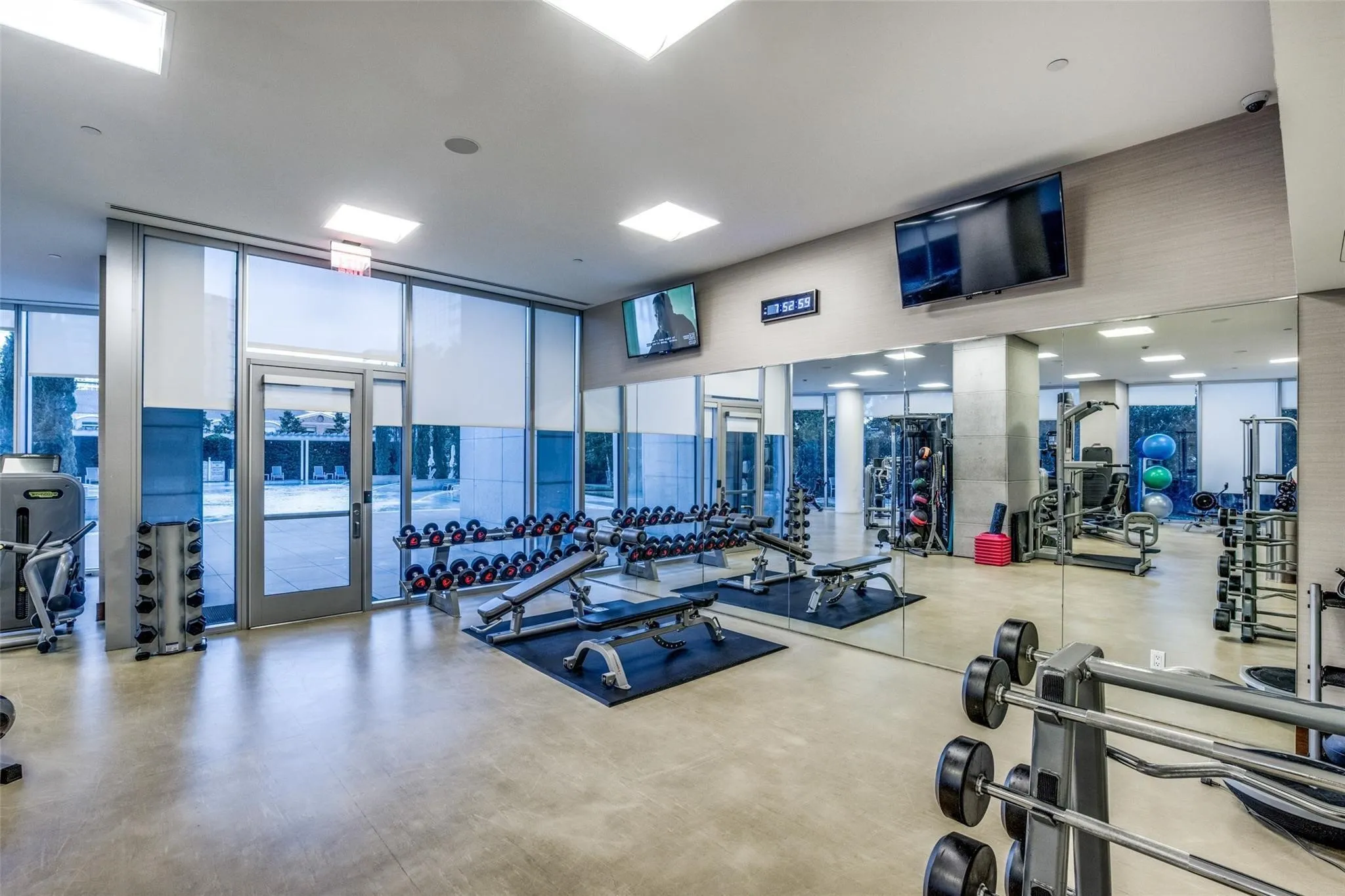 Fitness center featuring concrete flooring, full-height windows with roller shades, mirrored walls, and flush-mounted ceiling lighting
