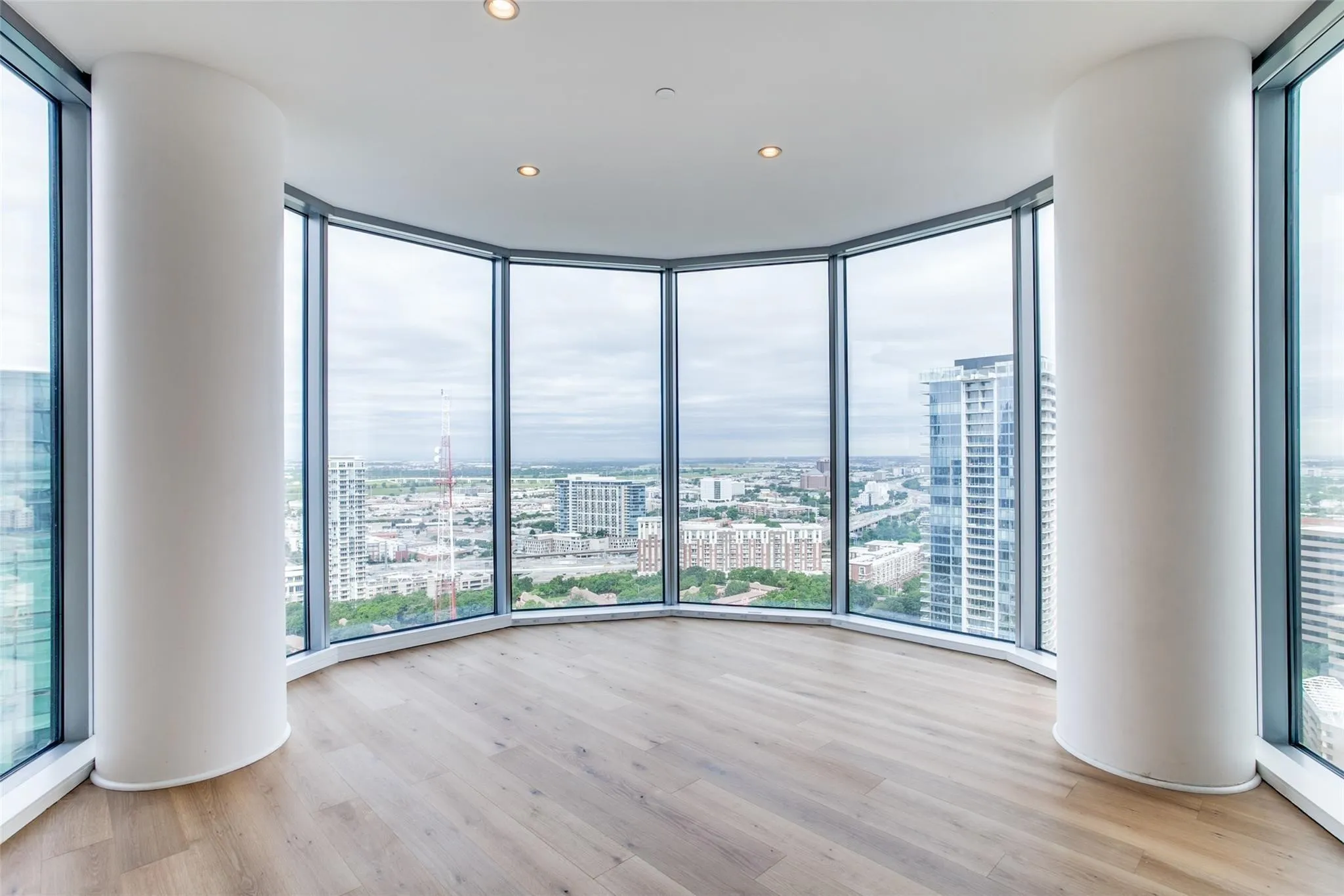 Expansive floor-to-ceiling windows, wood-finish flooring, recessed lighting, and curved architectural columns