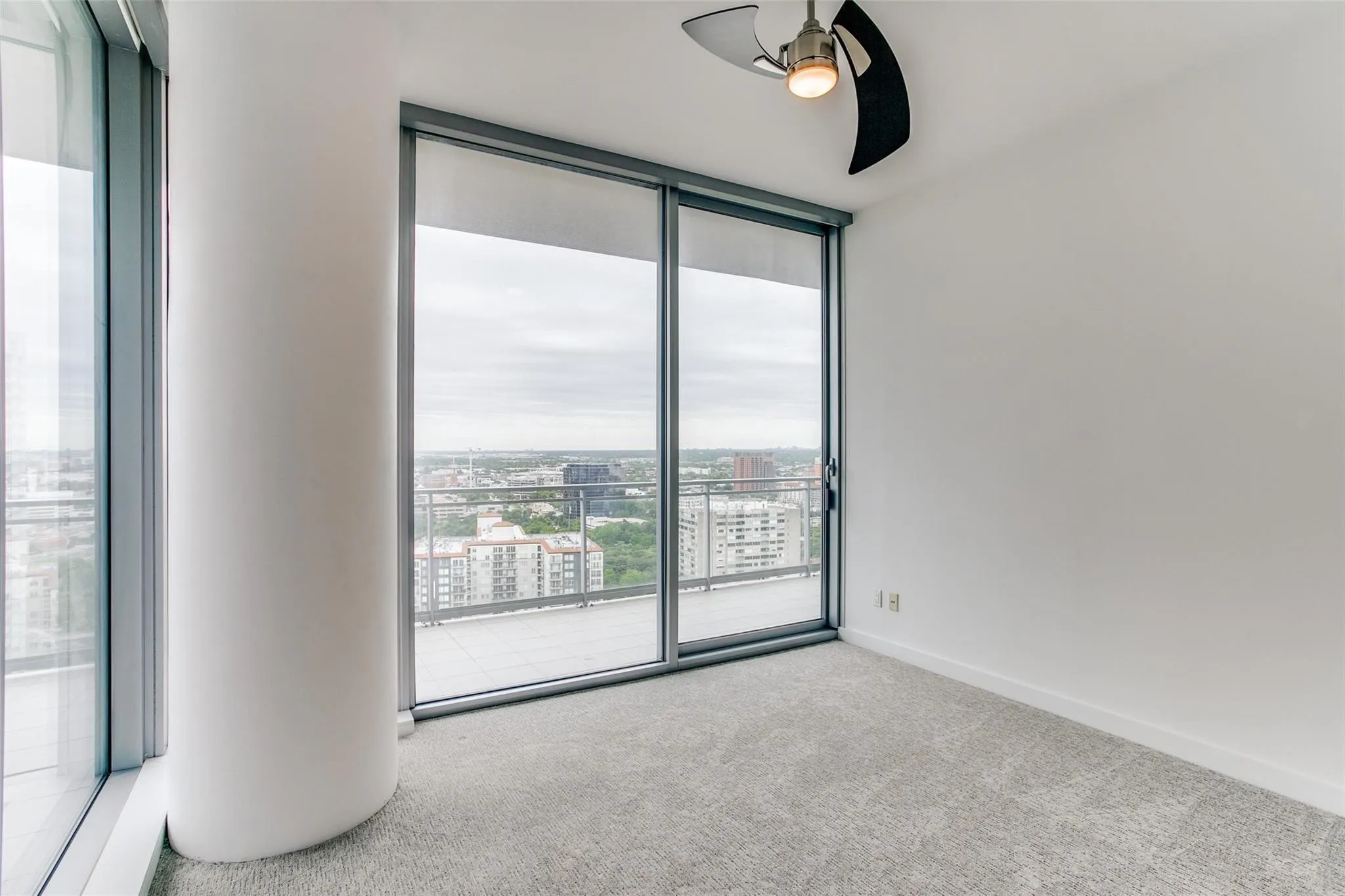 Floor-to-ceiling windows with roller shades, a private balcony, contemporary ceiling fan, and light grey carpet