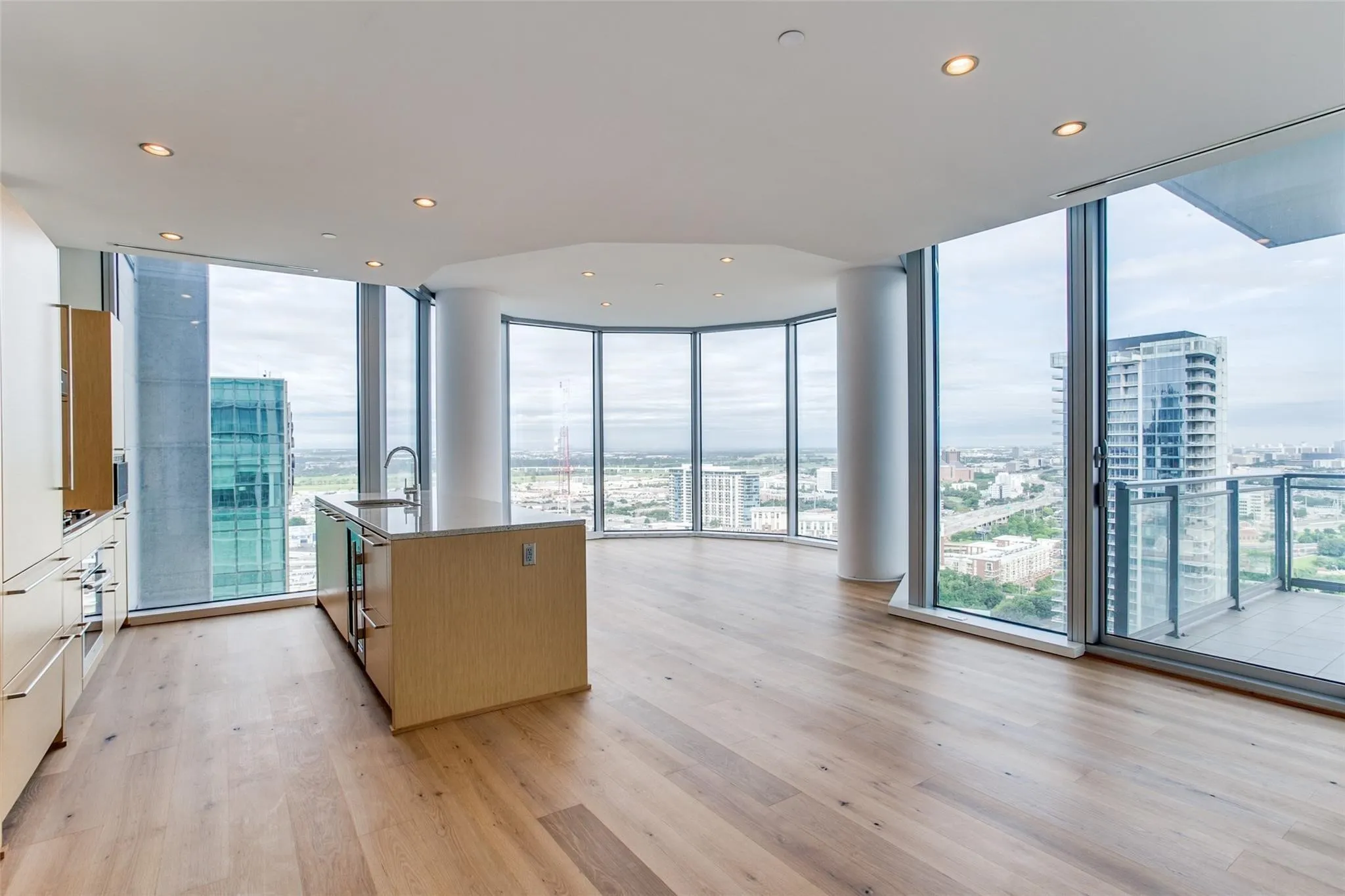 Open-concept living space with expansive floor-to-ceiling windows, wood-finish flooring, recessed lighting, and a kitchen island with a stainless steel sink