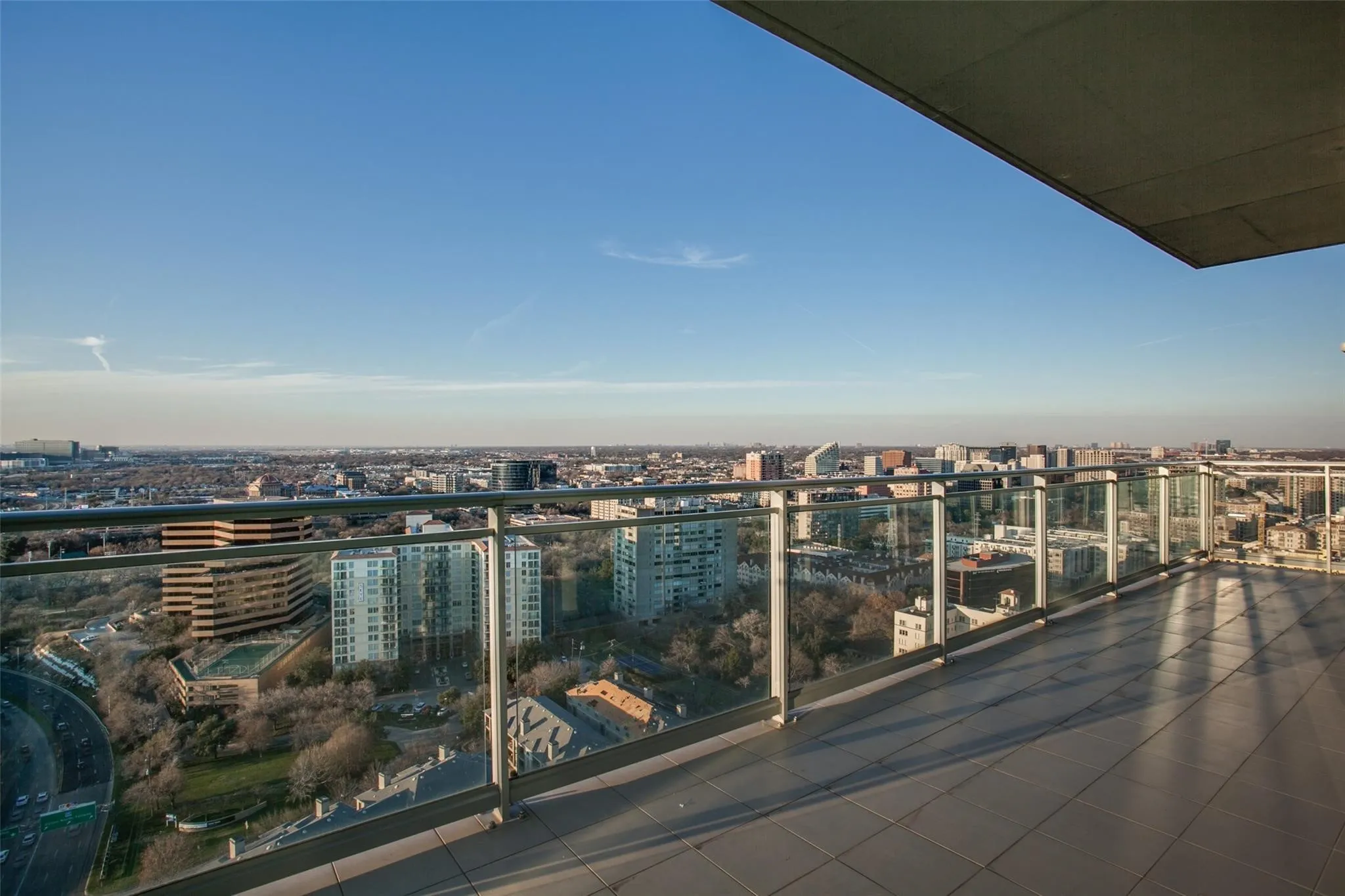 Expansive balcony featuring glass railings, tiled flooring, and an urban cityscape