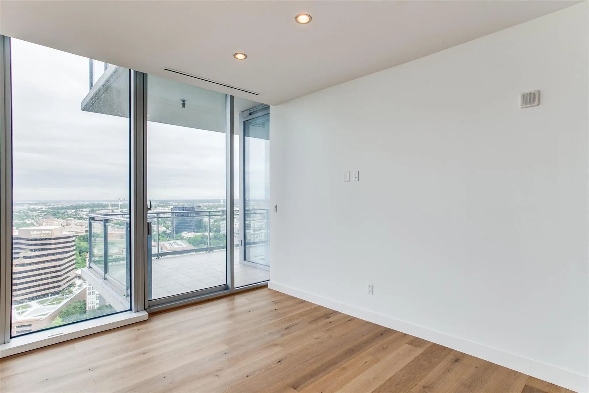 Floor-to-ceiling windows, wood-finish flooring, recessed ceiling lighting, and a private balcony with glass railings