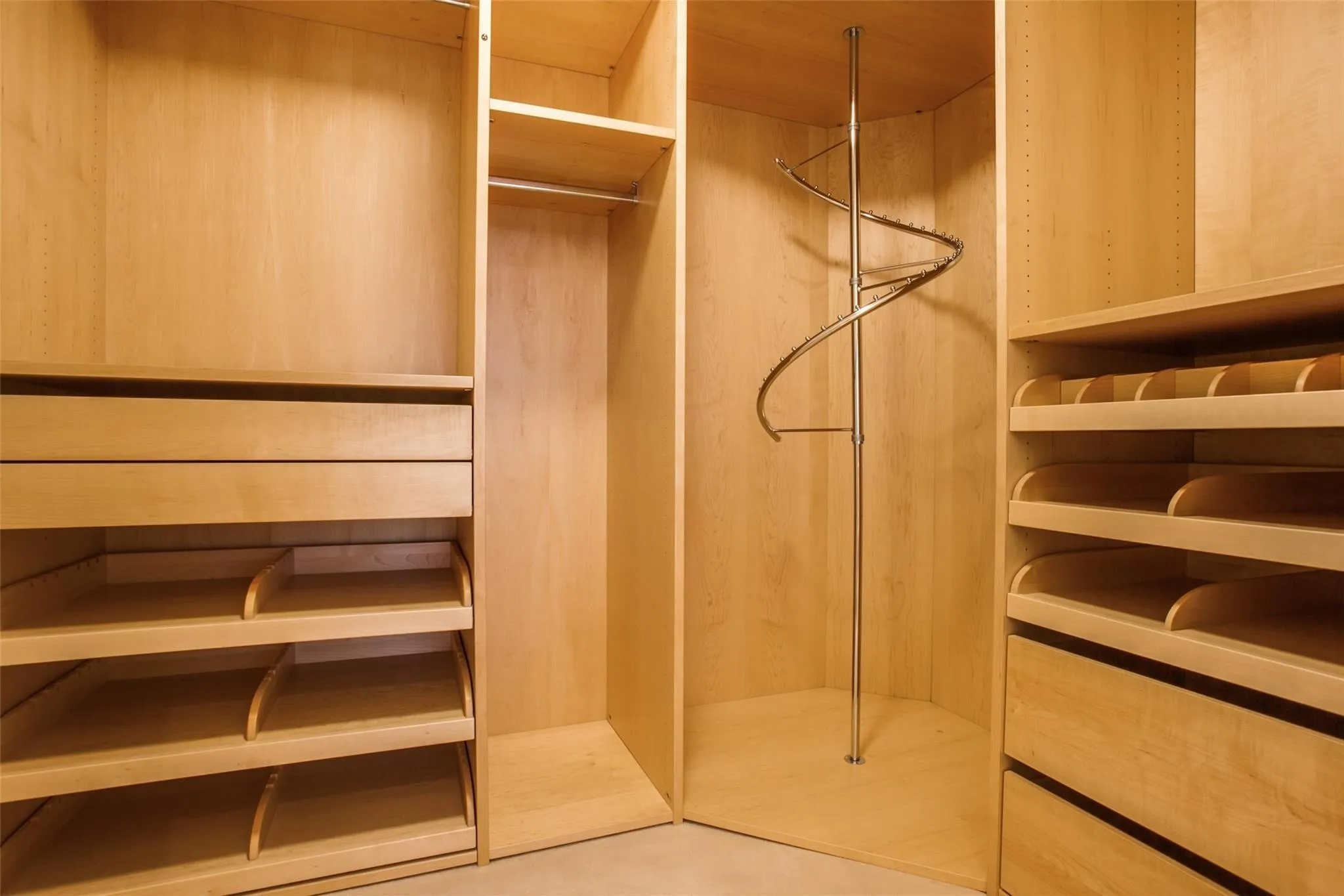 Built-in closet system featuring natural wood-finish cabinetry, integrated drawers, adjustable shelving, and a spiral garment rack