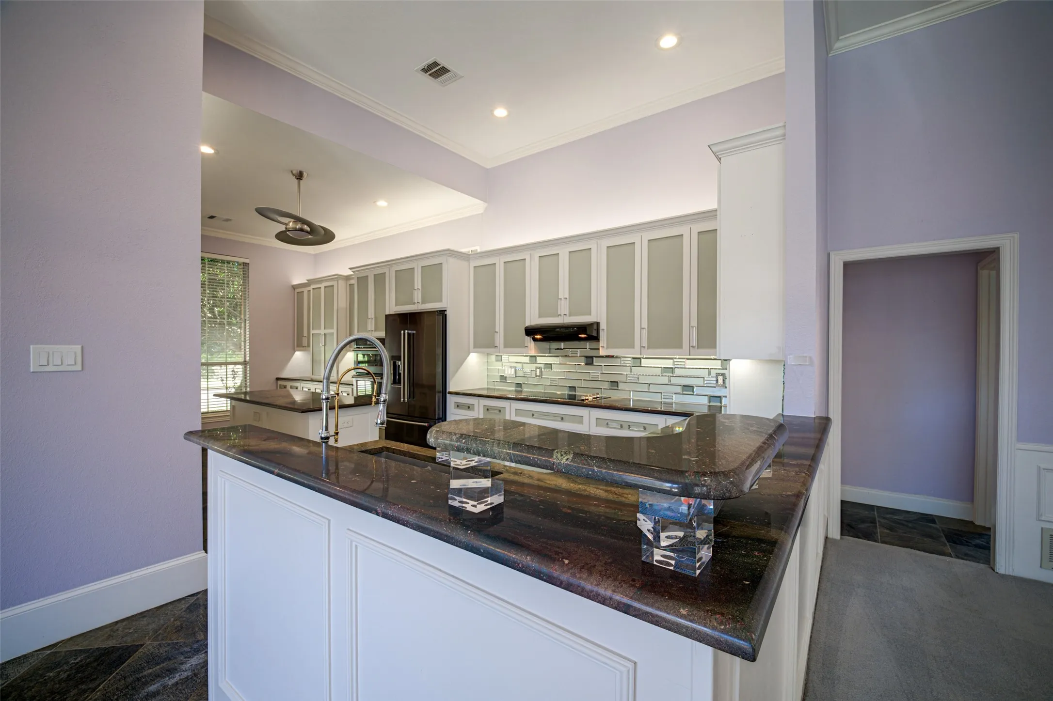 Kitchen featuring a peninsula with a dark countertop, white paneled cabinetry, stainless steel faucet, and a subway tile backsplash