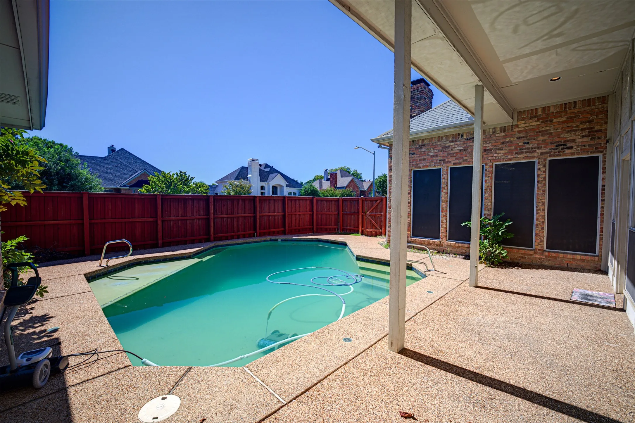 In-ground pool, expansive aggregate patio, covered patio area, brick exterior, and wood privacy fencing
