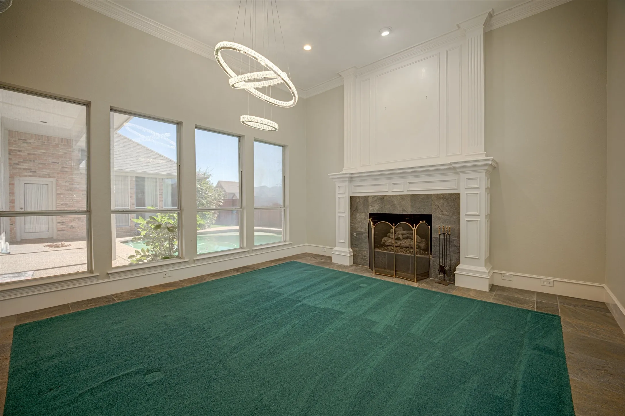 Soaring ceilings and a decorative chandelier illuminate the space, complemented by a white mantel fireplace with a stone surround