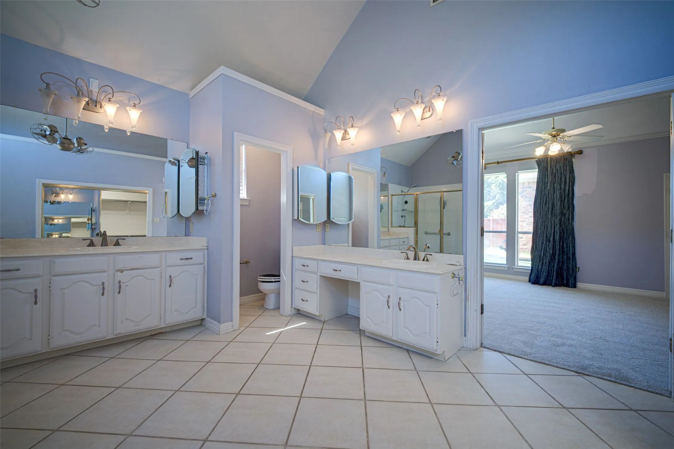 Dual vanity sinks, tile flooring, vaulted ceiling, and ample counter space with built-in storage