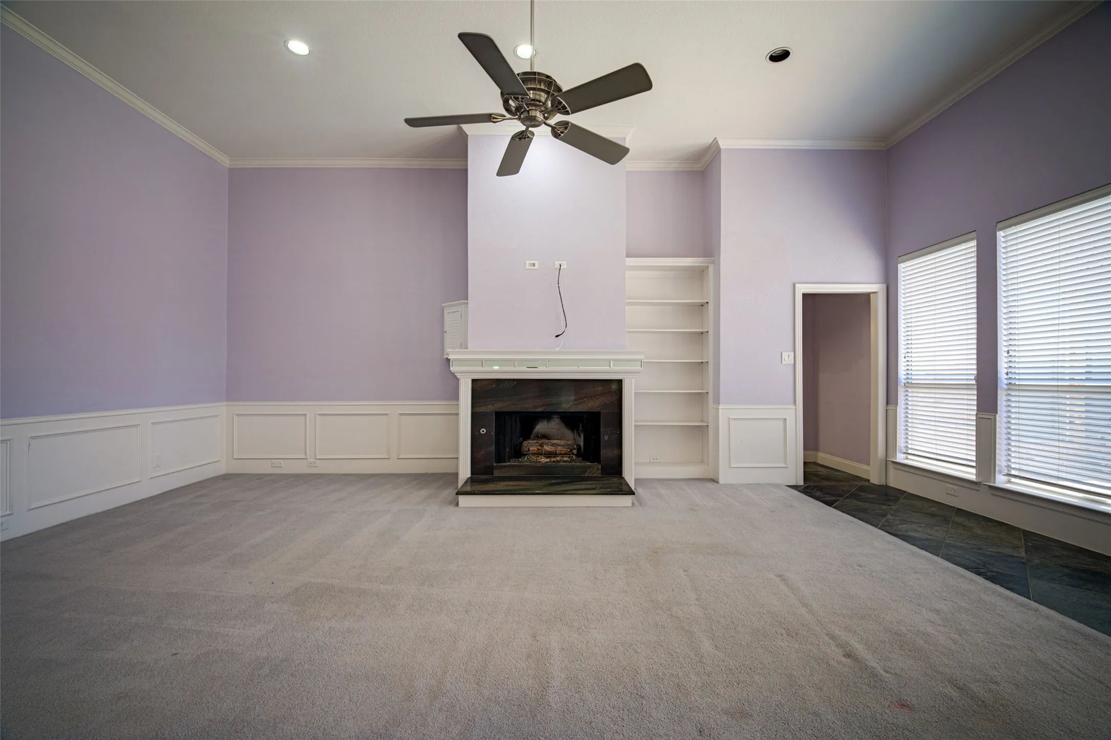 Recessed lighting, ceiling fan, fireplace with dark stone surround, integrated shelving, and dual windows with blinds