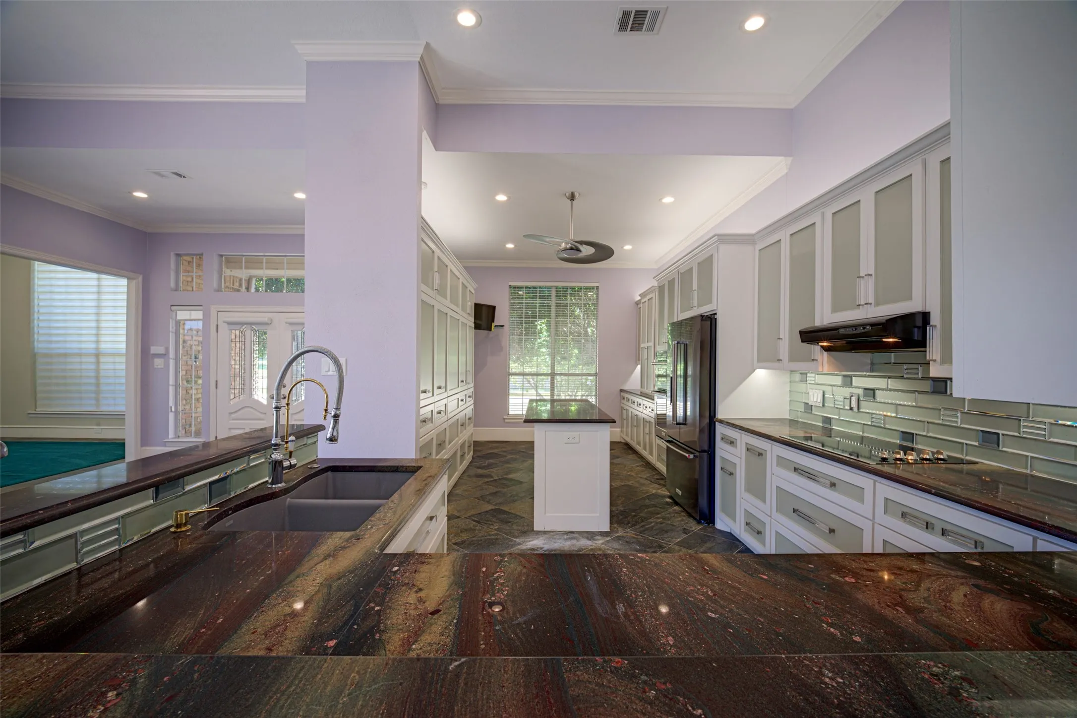 Kitchen featuring dark multi-toned countertops, a double basin sink with a gooseneck faucet, light-colored cabinetry with frosted glass inserts, a subway tile backsplash, and recessed lighting